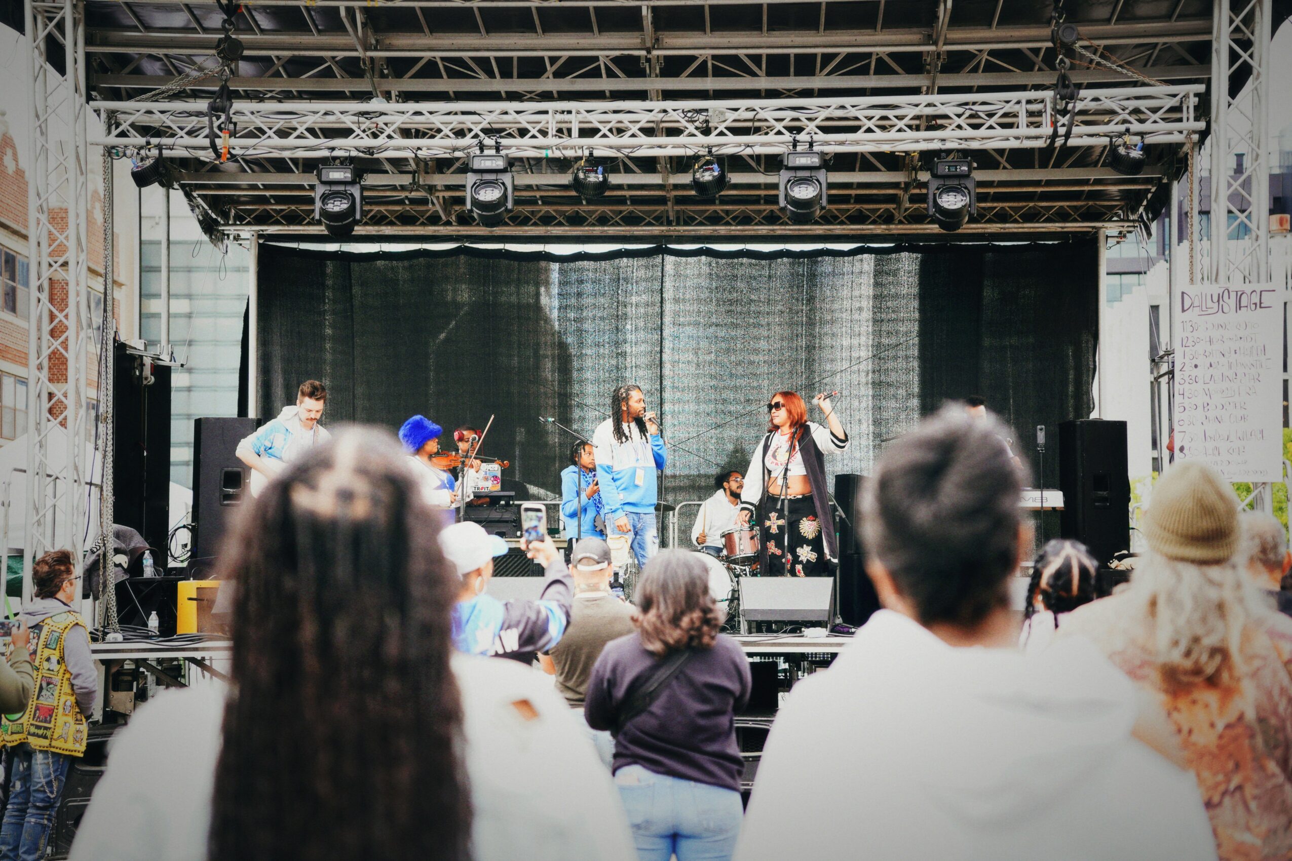 Band performing on stage with audience watching, stage with lighting and backdrop, indoor concert setting.