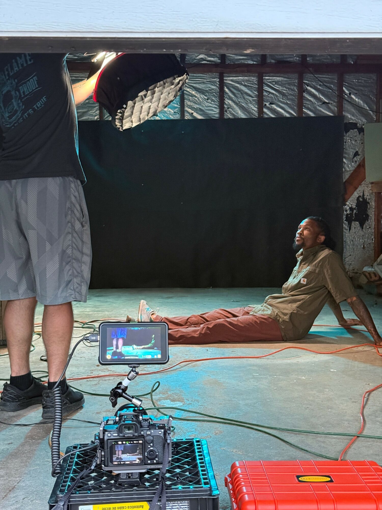 Person sitting on the floor with equipment and cables, in a room with a black backdrop and metal walls.