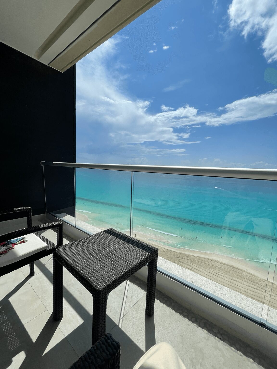 Balcony with black chairs overlooking a beach and ocean under a partly cloudy sky.