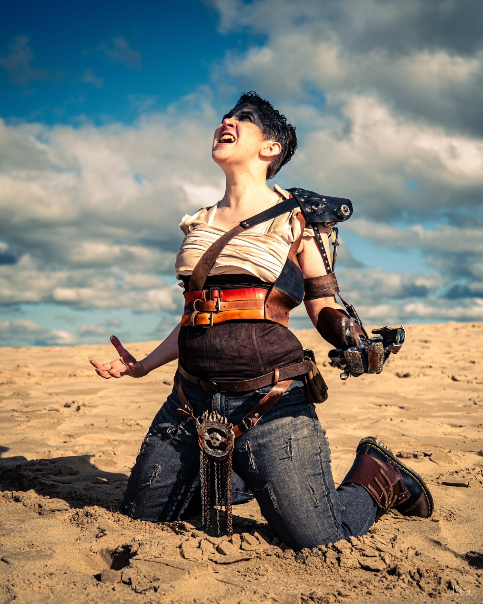 Woman kneeling on sand, smiling and looking up, with a cloudy sky background.