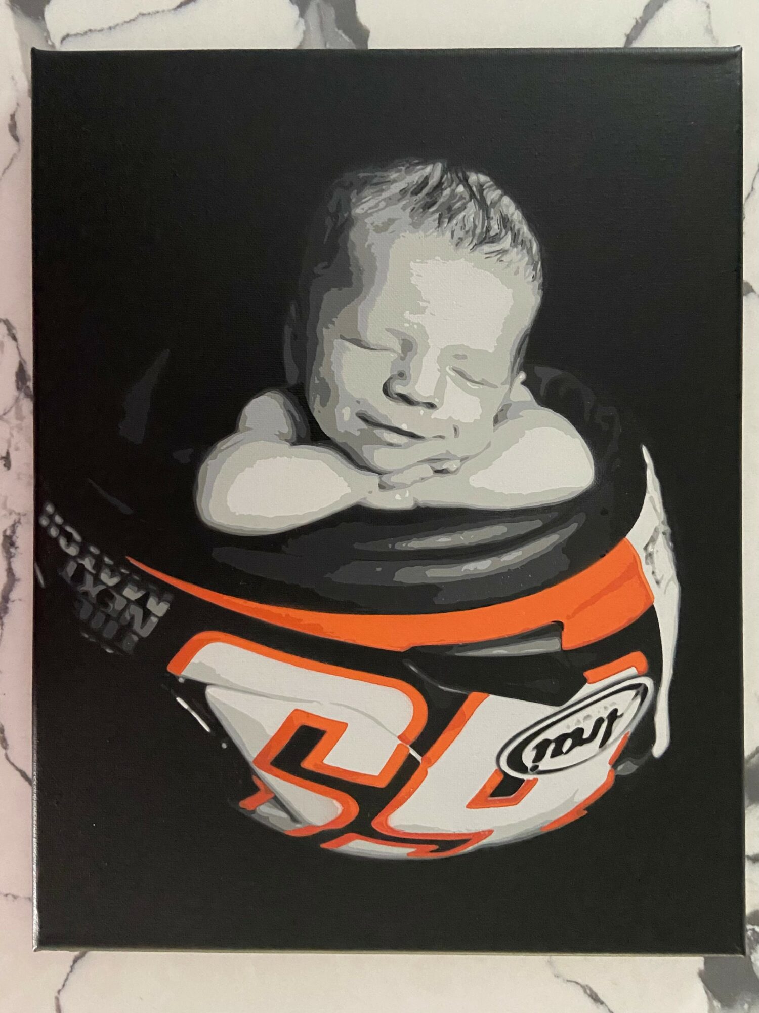 Black and white photo of a sleeping baby resting on a sports helmet with orange and white details.