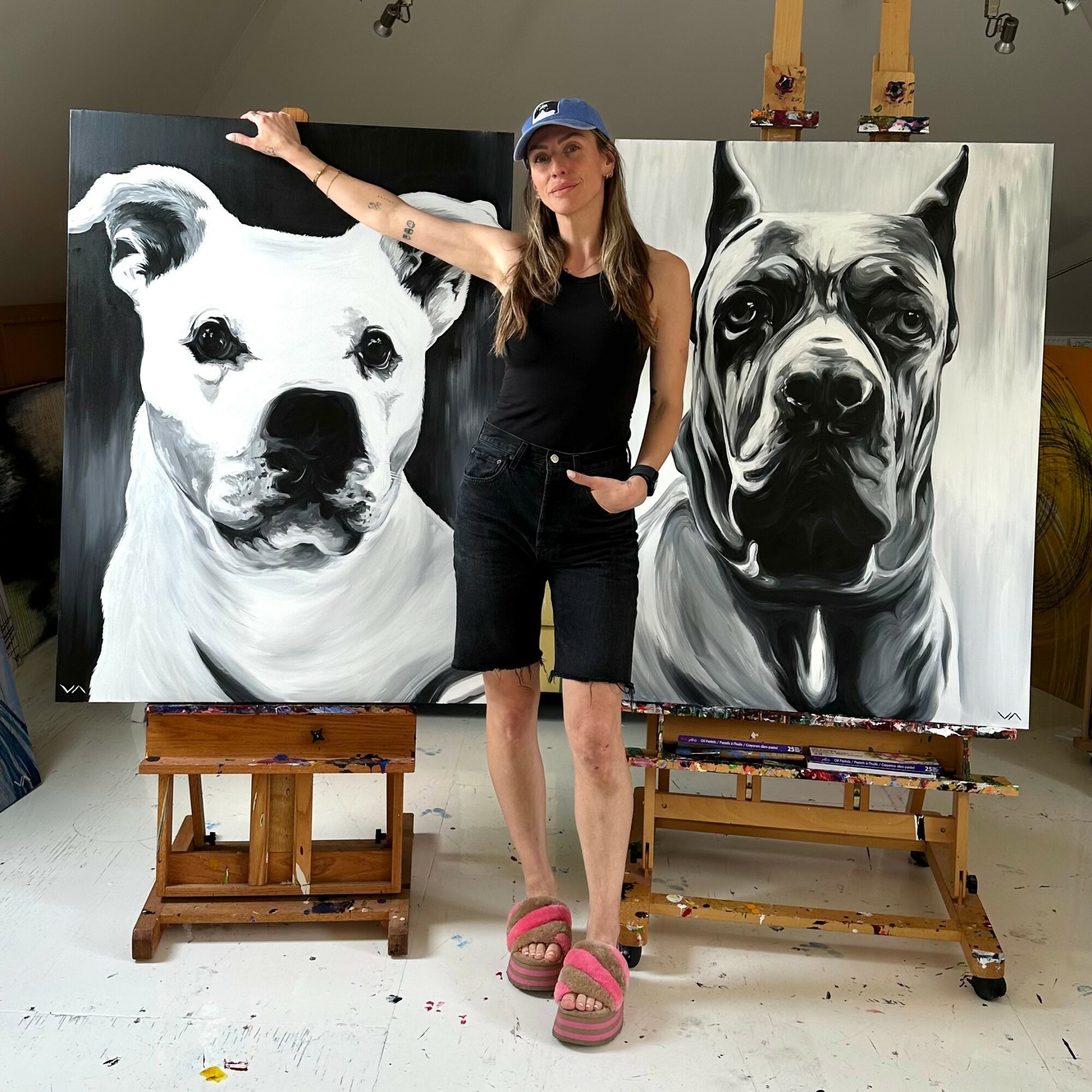 Woman standing between two large black and white dog portraits, one on each side, in an art studio.