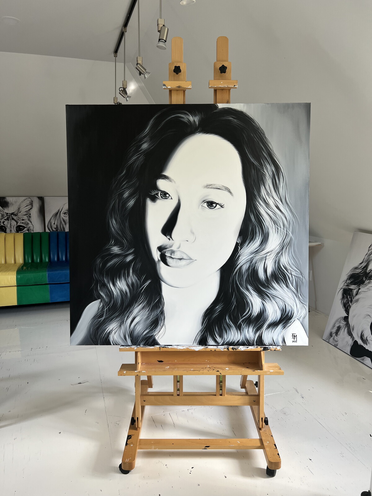 Black and white portrait of a woman with wavy hair, looking slightly to the side, on an easel in a room.