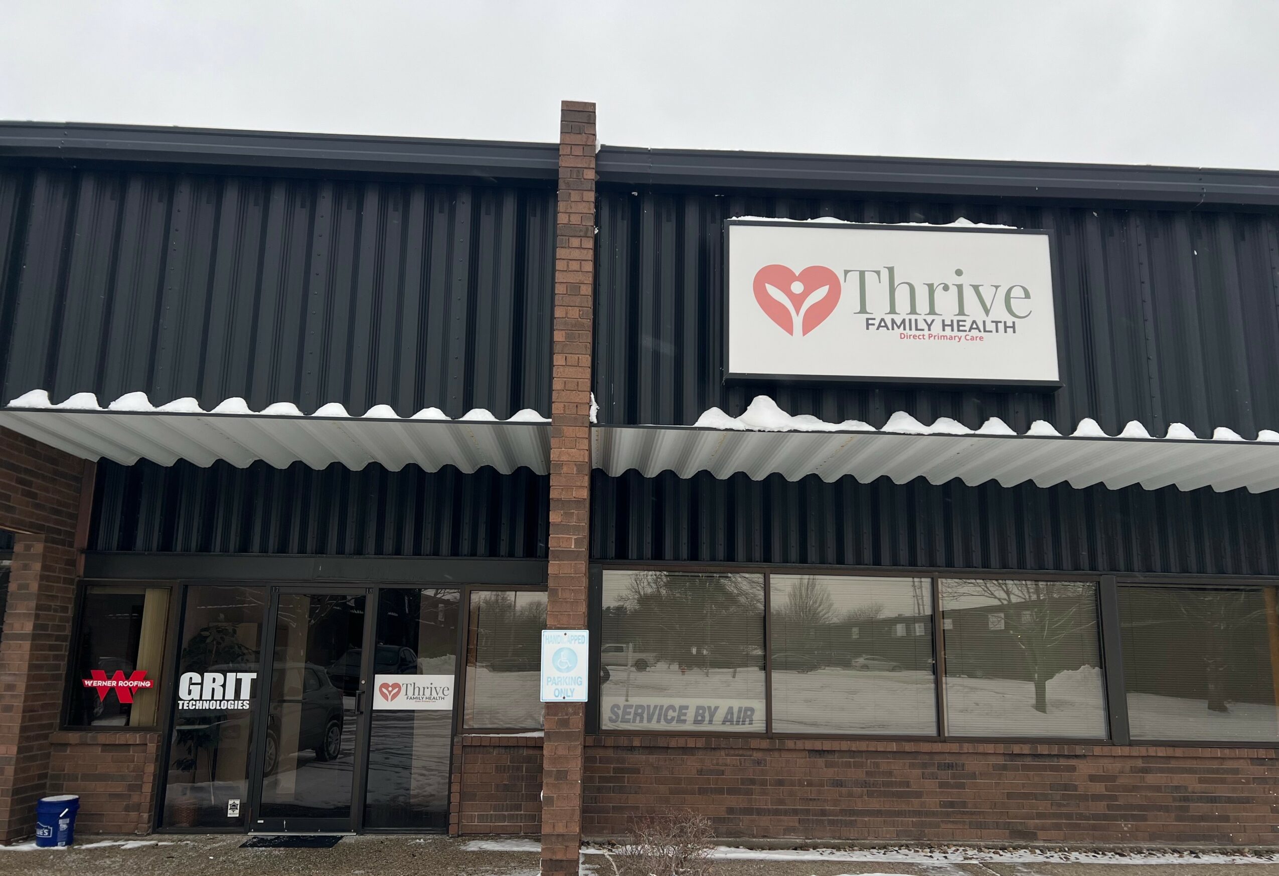 Exterior of a building with a sign reading 'Thrive Family Health' and a logo, glass doors, and windows.