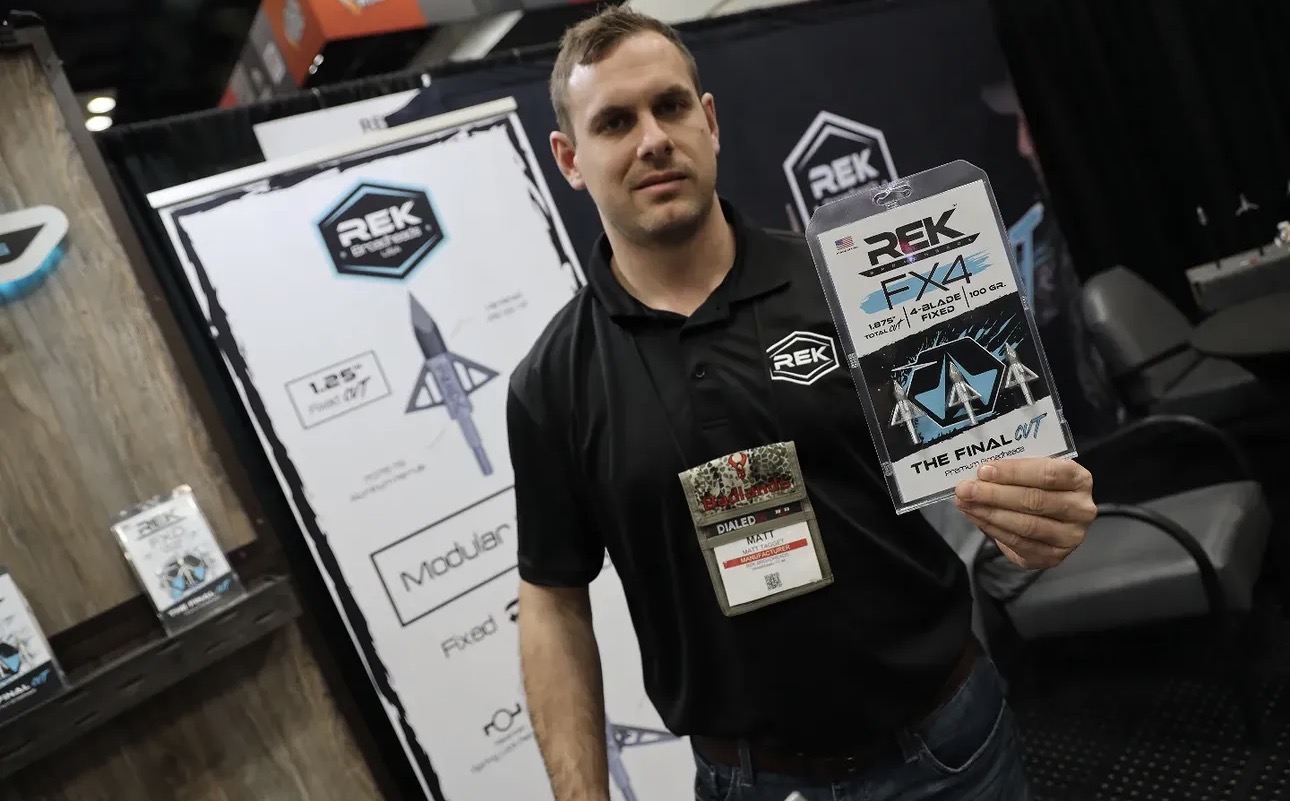 Man holding a trophy at a convention booth with banners in the background.