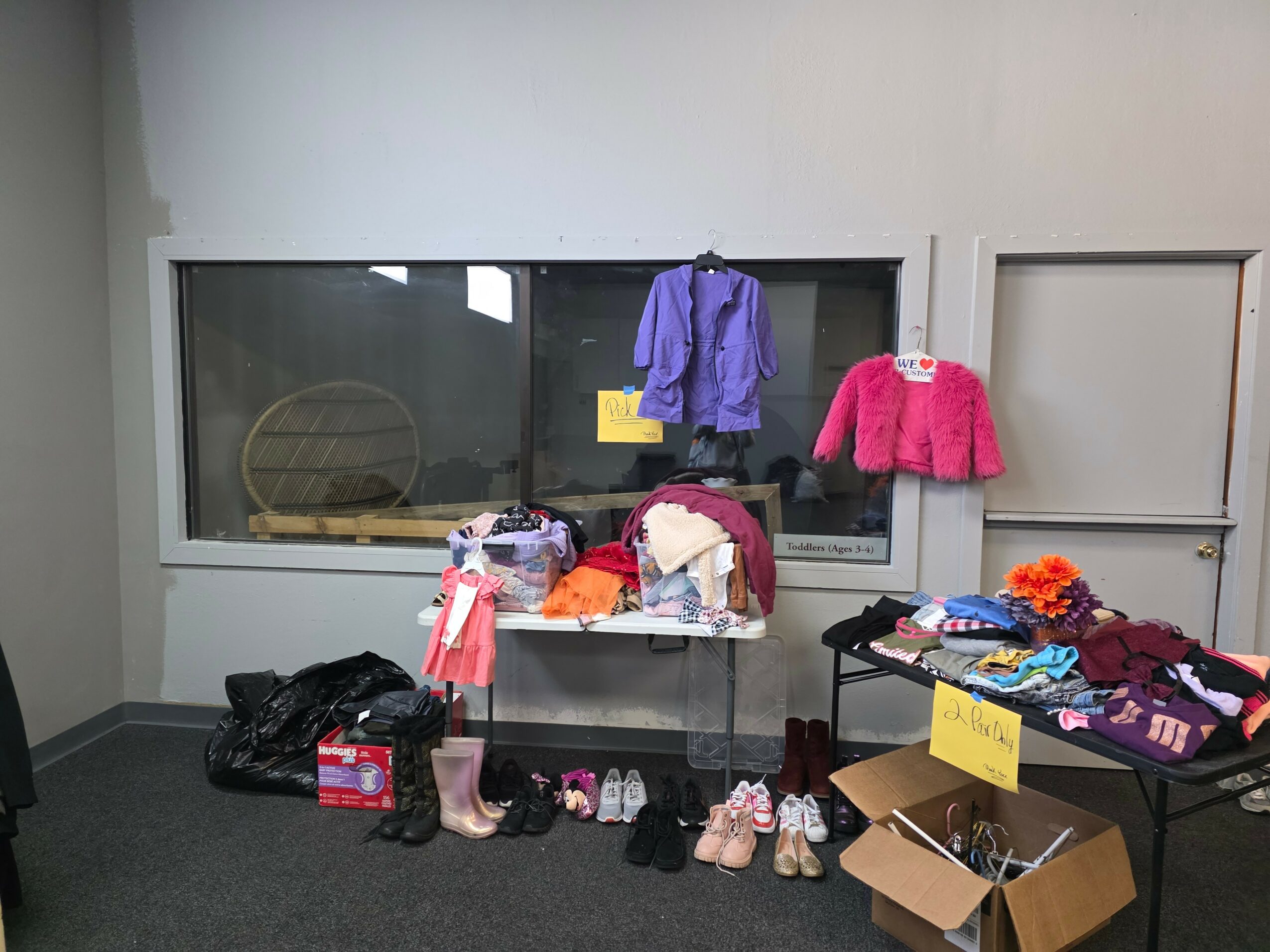 Clothing and shoes displayed on a table and window ledge, with a cardboard box and bags nearby.