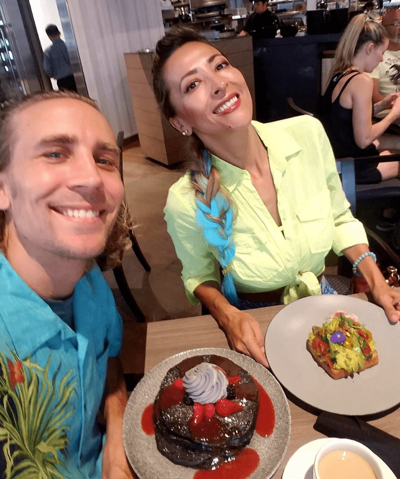 Two people smiling at a table with desserts, one woman with a braid and a man in a blue shirt, in a restaurant.