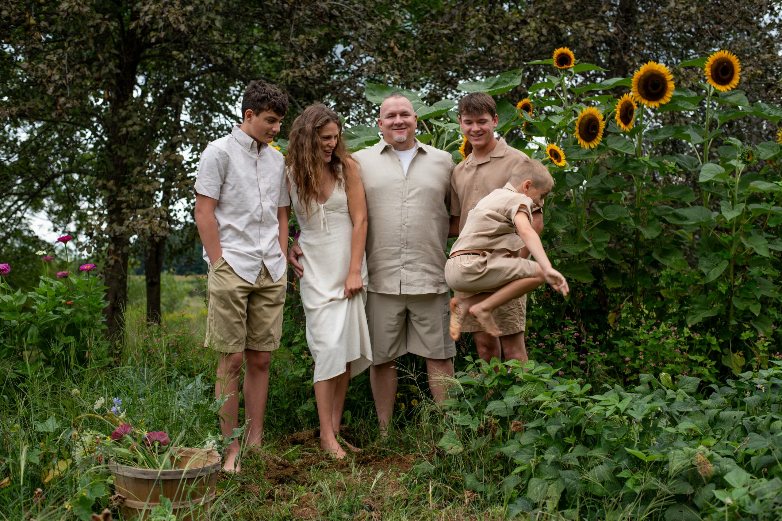 Group of five people standing outdoors near sunflowers and trees, smiling and posing for a photo.