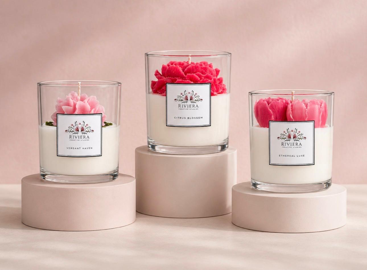 Three candles with pink and red flowers in glass containers on round bases, against a soft pink background.