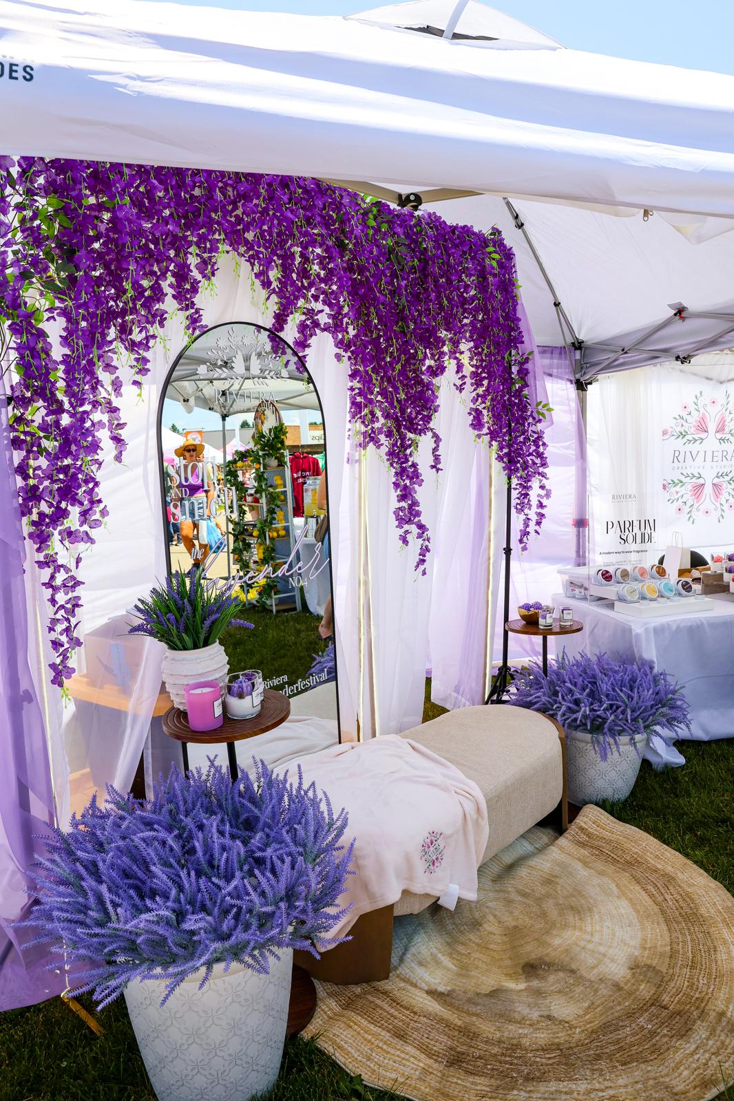 Decorated tent with purple flowers, mirror, and seating area, featuring potted plants and a woven rug.