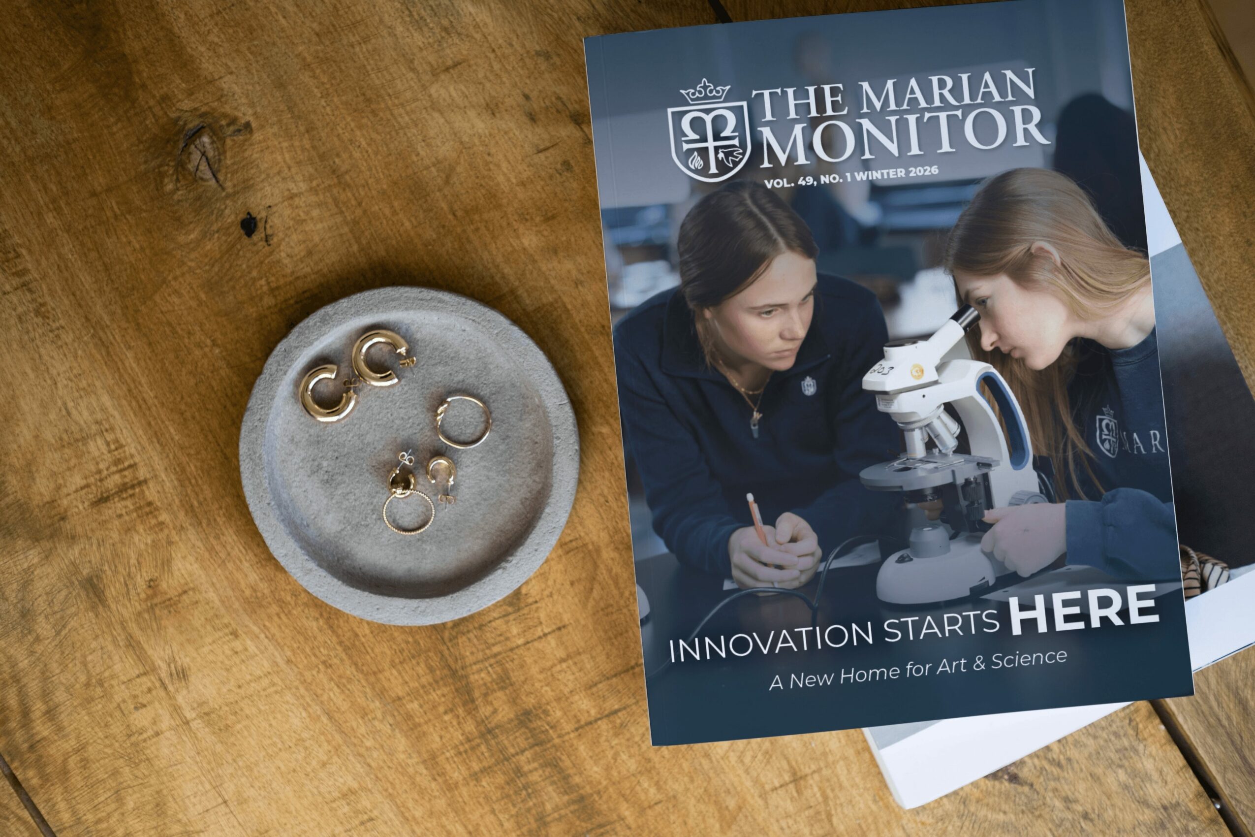 Brochure titled 'The Marian Monitor' with two young women looking through a microscope, on a wooden surface.