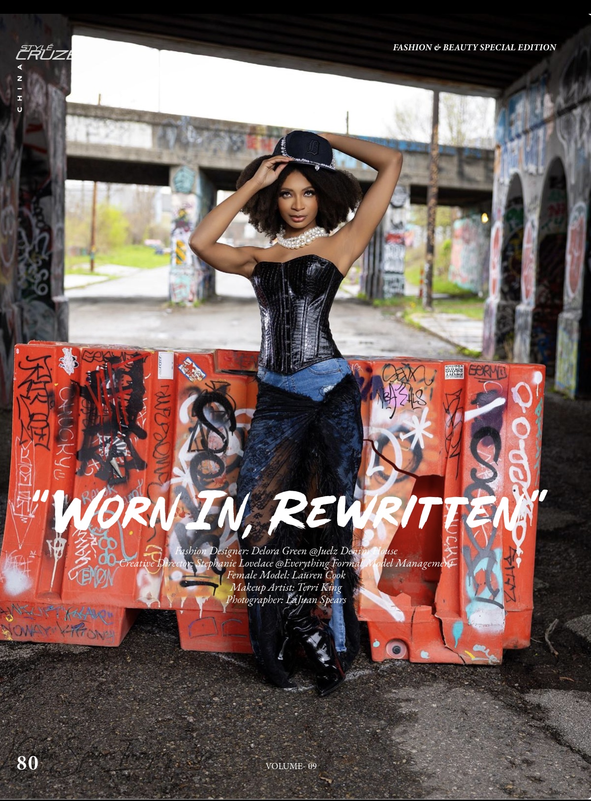 Woman in a black corset and jeans poses under a bridge with graffiti-covered walls behind her.