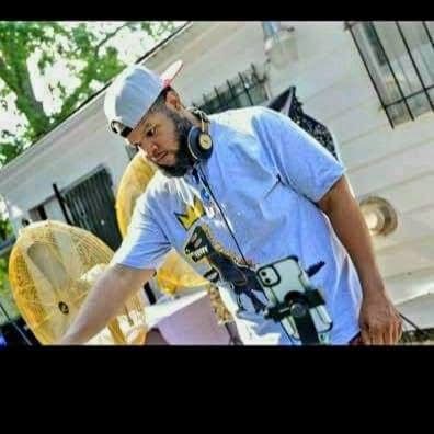 Young man wearing a light blue shirt, white cap, and headphones, standing outdoors near a fan and a fence.