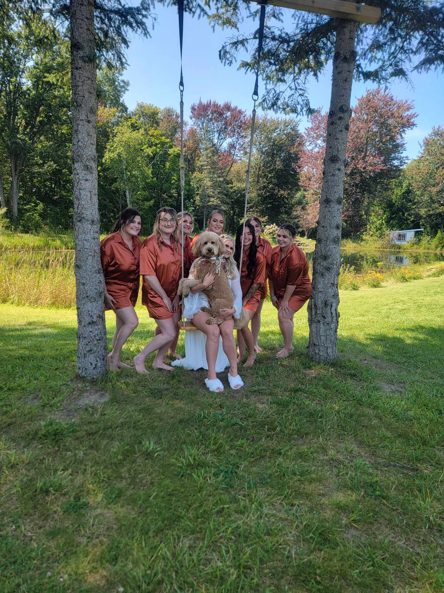 Group of five people, four women and one girl, sitting on a swing in a park with trees and grass, sunny day.