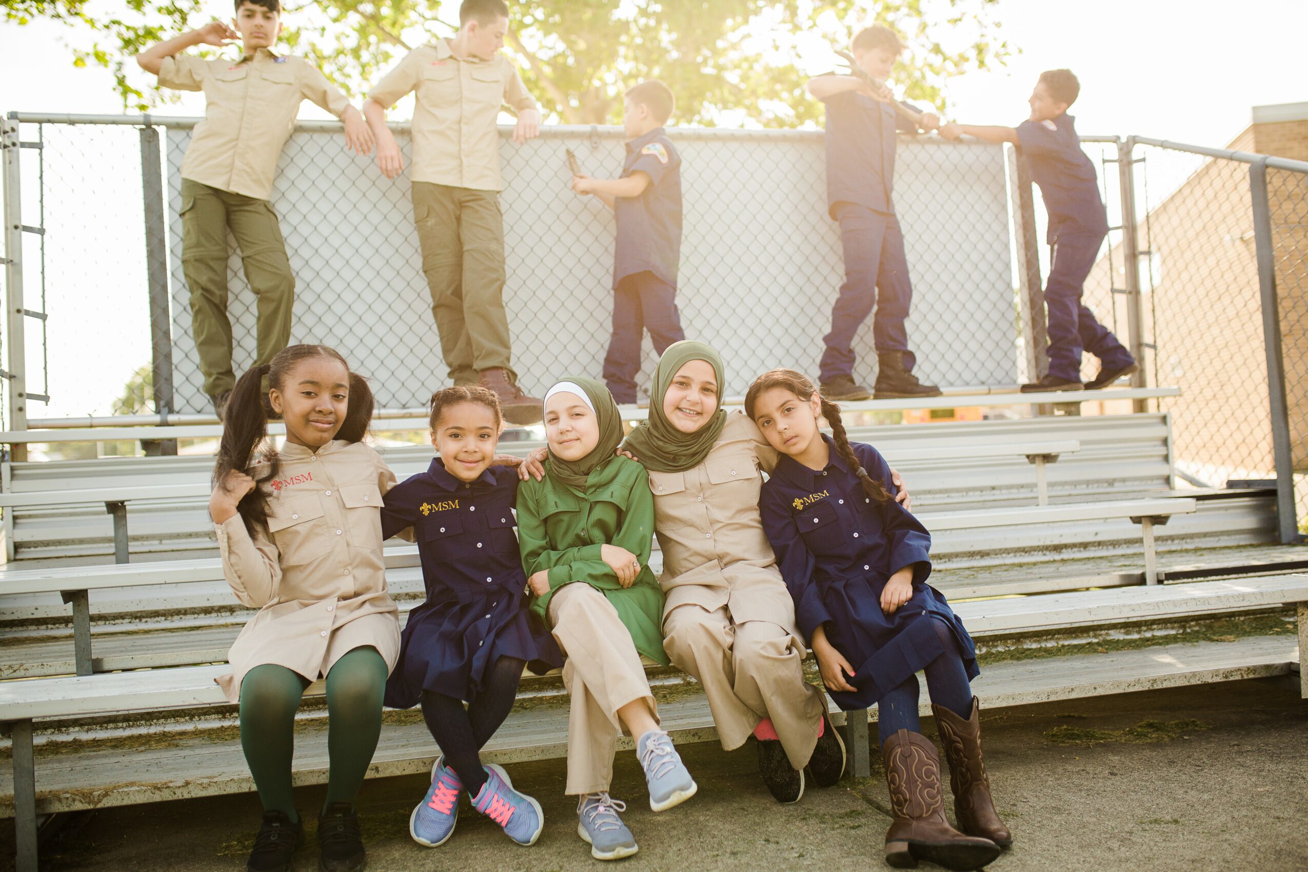 Group of children sitting on bleachers outdoors, some standing behind, smiling and posing for the photo.