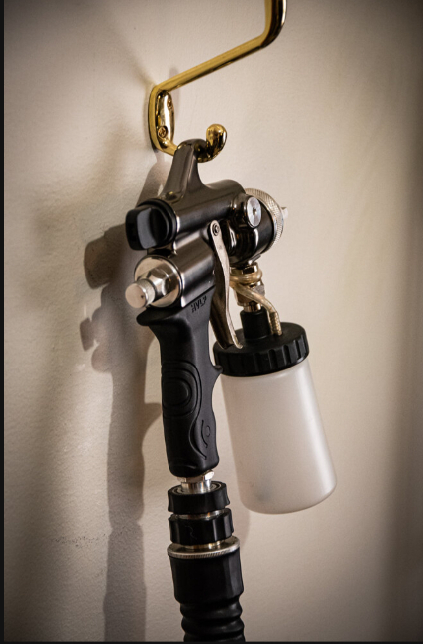 Medical spray gun hanging on a wall with a white container attached, viewed from the side.