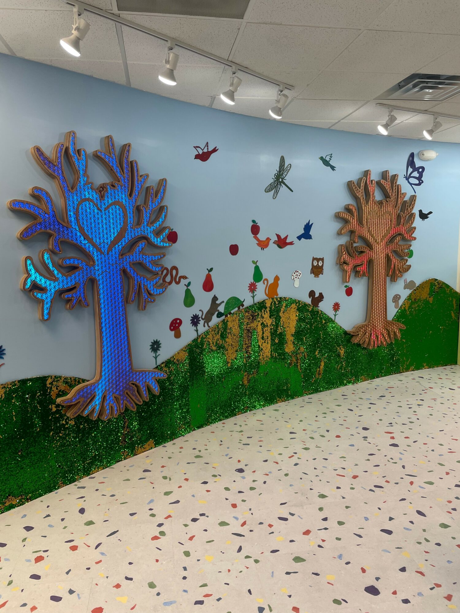 Decorative wall with two large trees, colorful butterflies, and a green hill, in a bright indoor space.