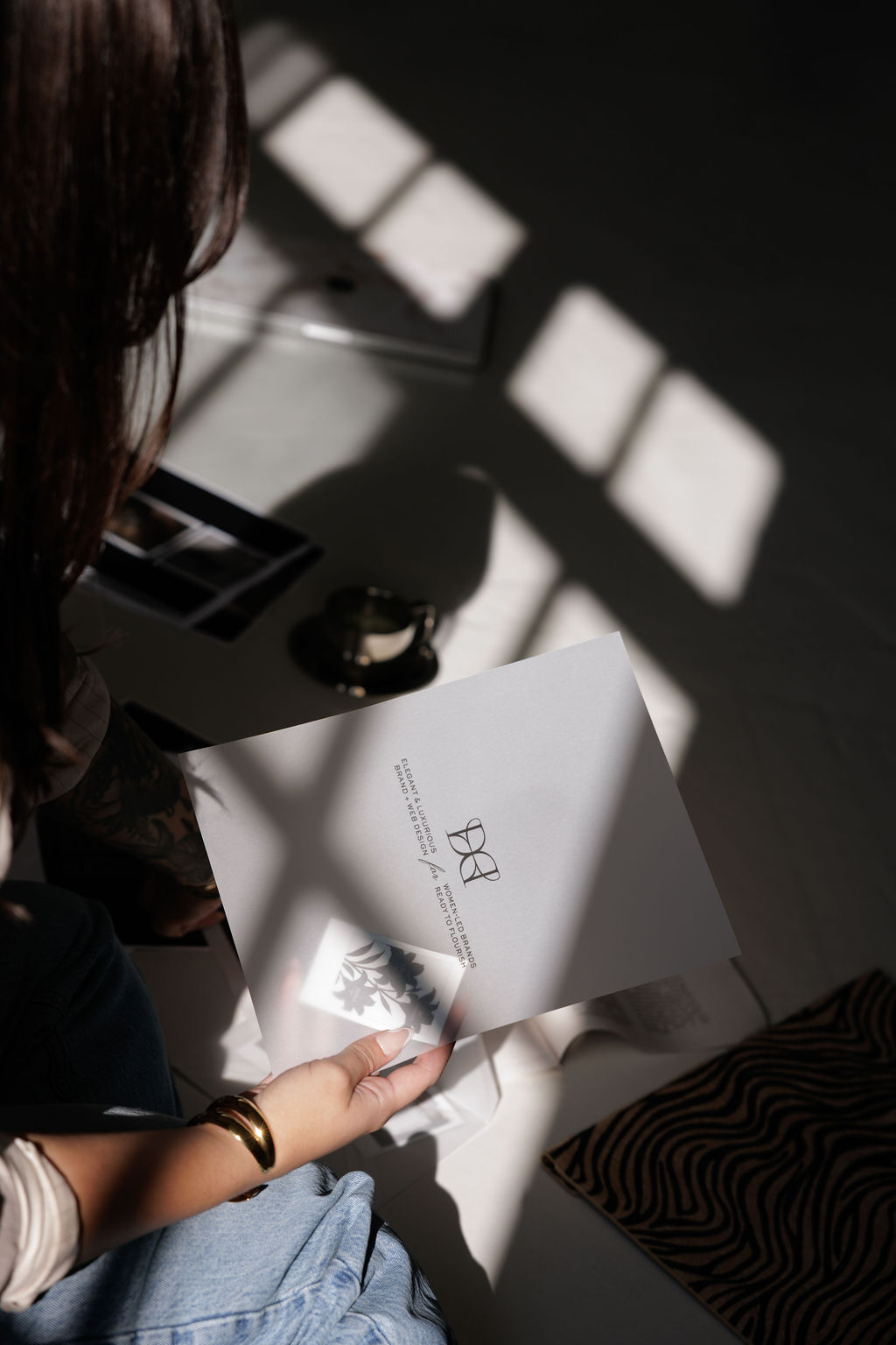 Person holding a paper with text, sunlight casting shadows on the surface, part of a striped cushion visible.
