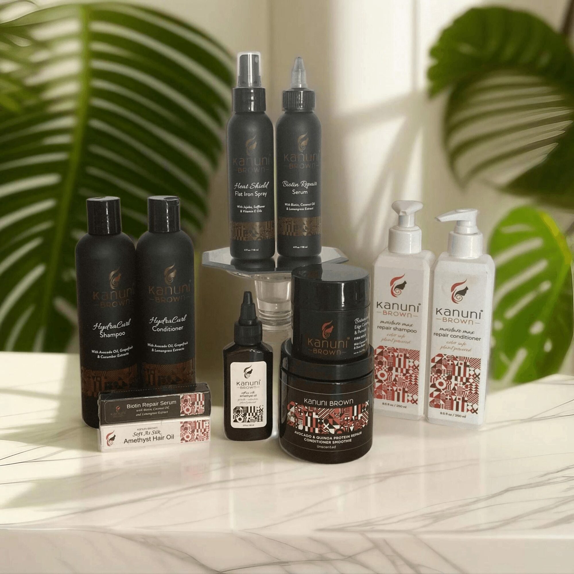 Collection of hair care products including sprays, serums, and creams on a marble surface with green leaves in background.