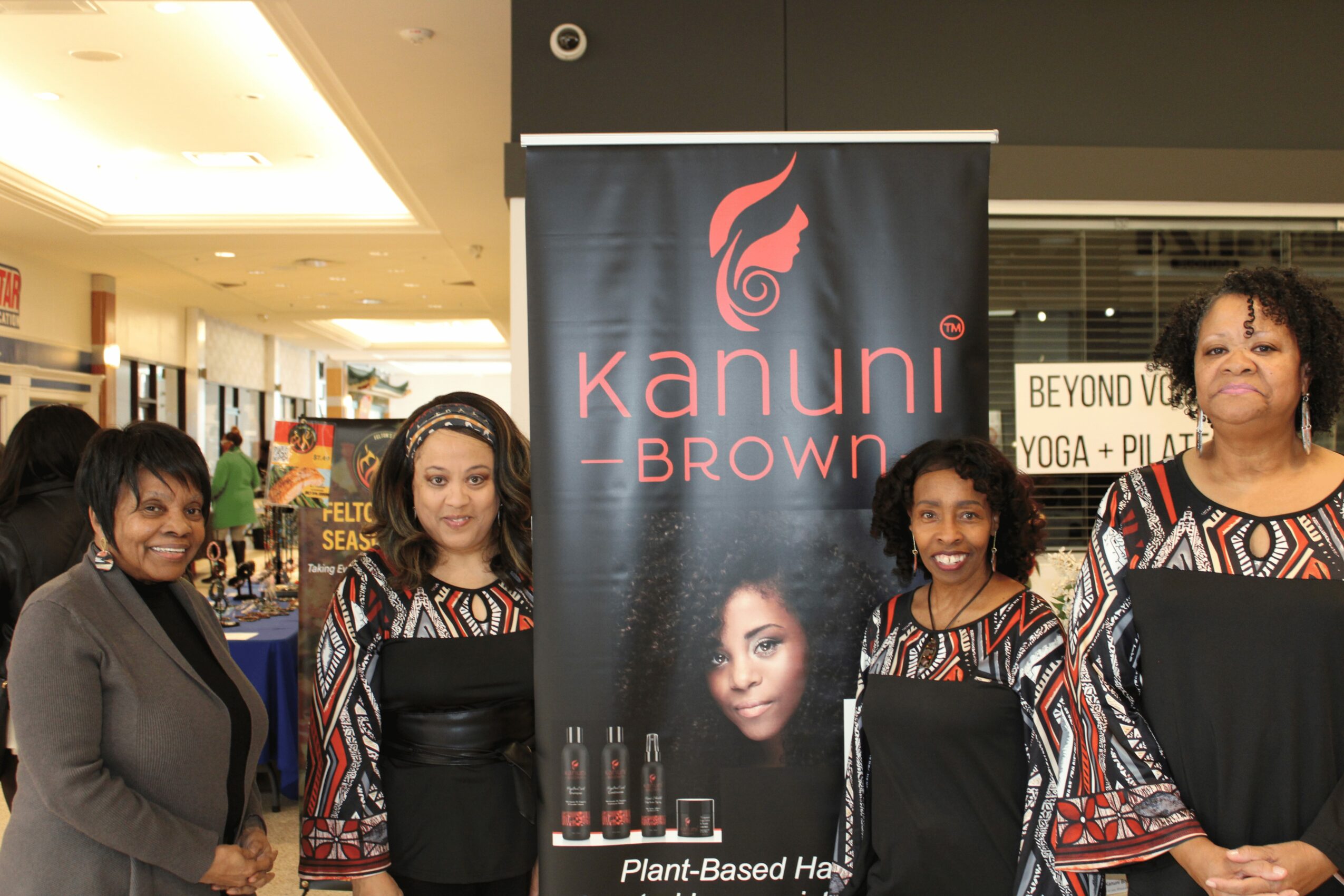 Four women stand in front of a Kanuni Browz banner in a shopping mall, smiling and posing for the photo.