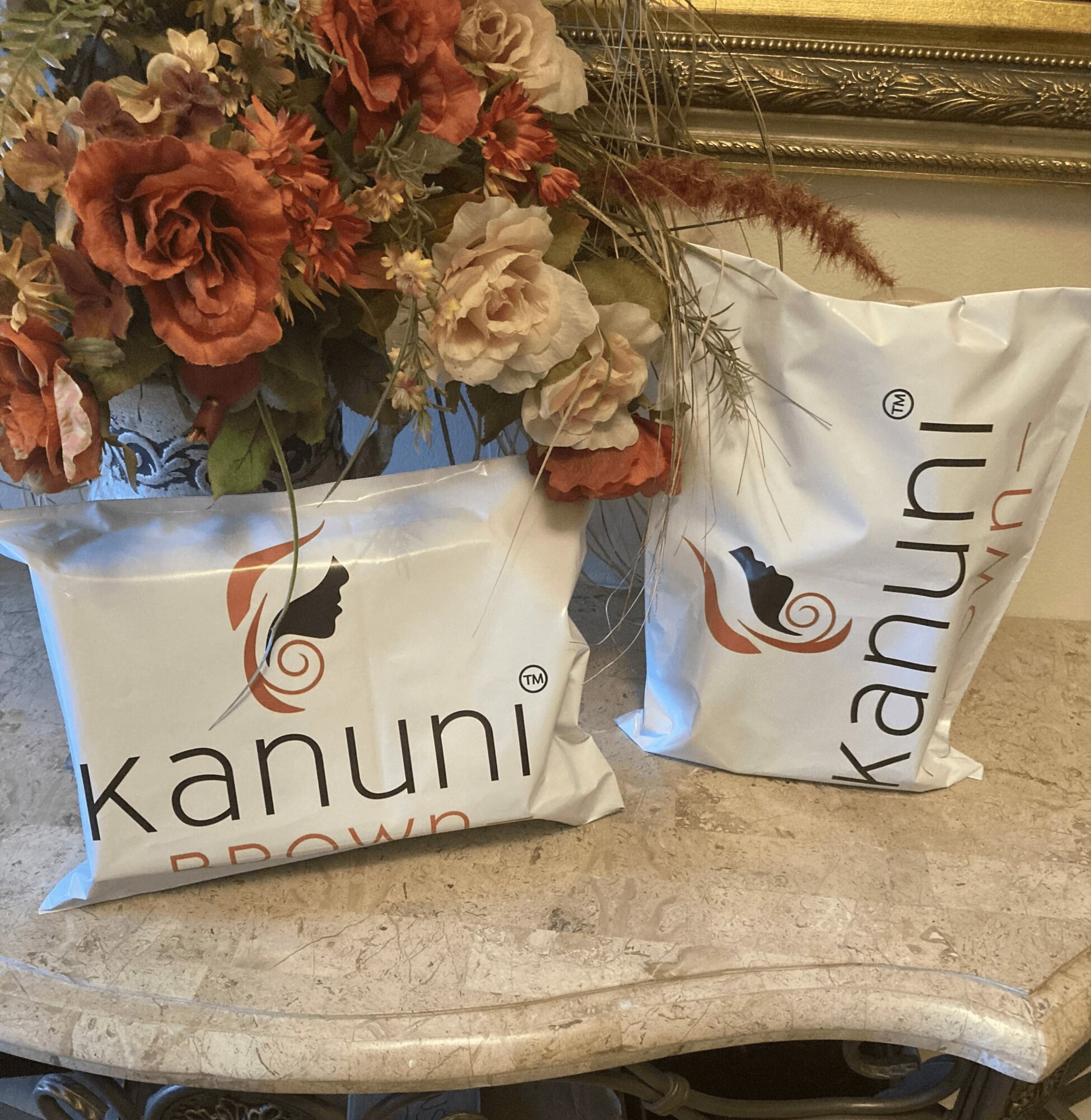 Two packages of Kanuni brown rice on a marble surface with a flower arrangement behind them.