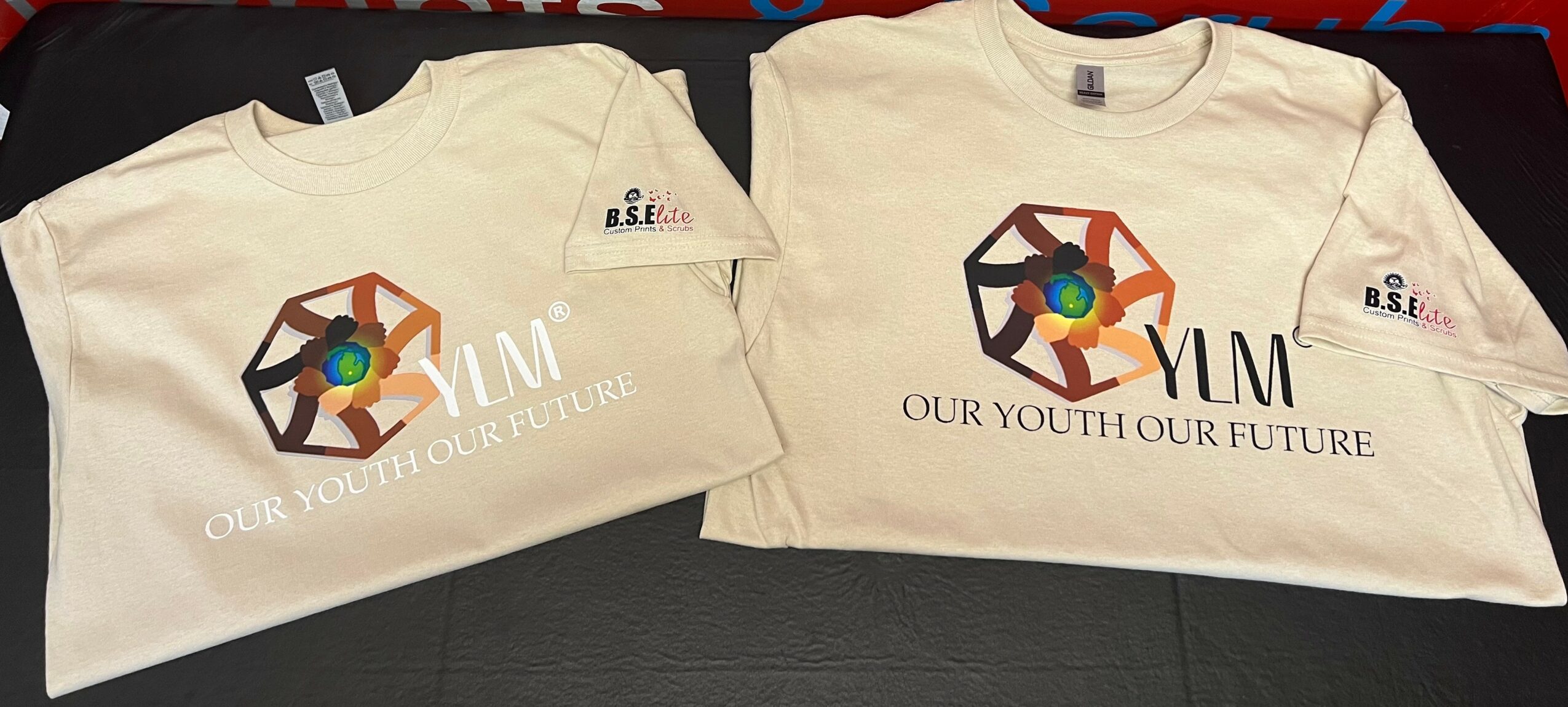 Two white T-shirts with a colorful geometric logo and the text 'YLM' and 'OUR YOUTH OUR FUTURE' printed on them.