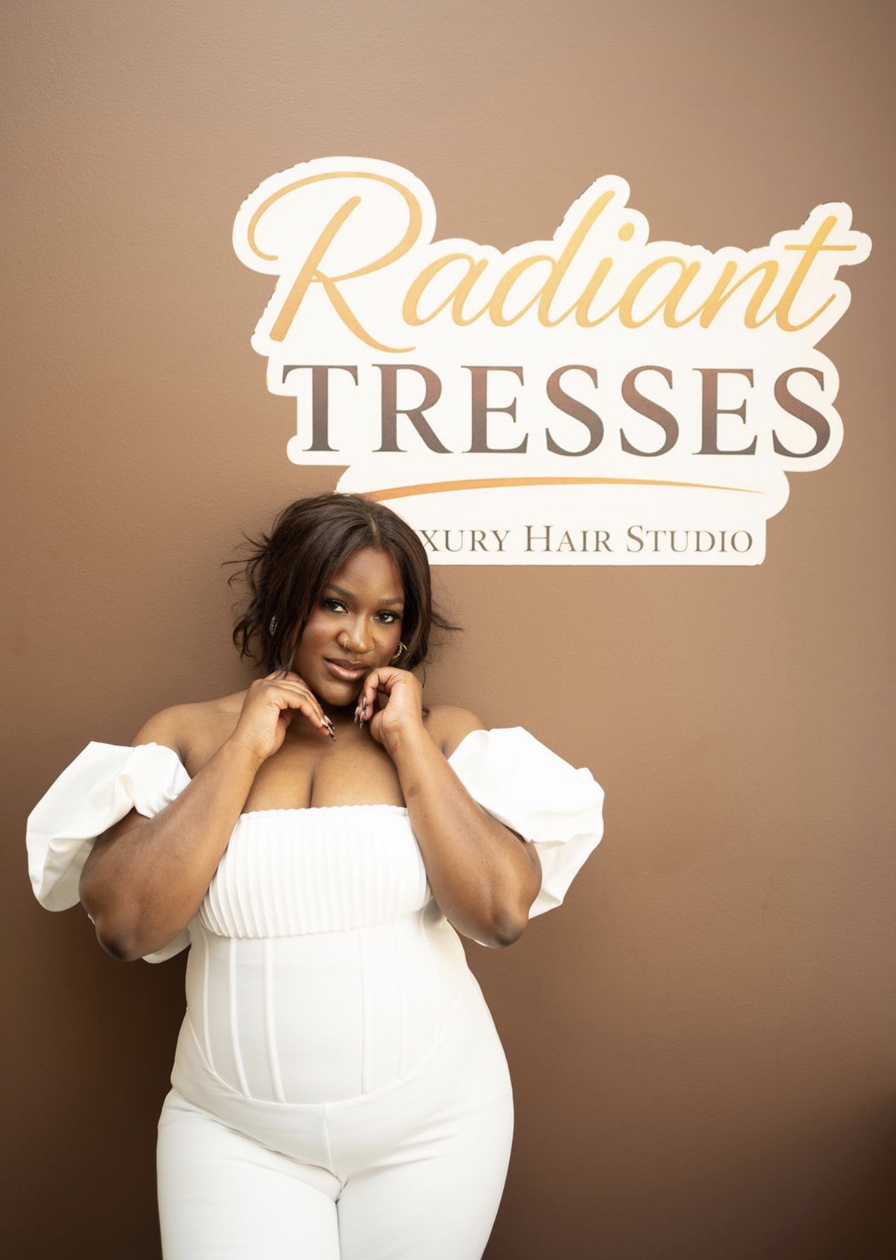 Woman with short hair in white outfit standing in front of a sign that reads 'Radiant Tresses Luxury Hair Studio'.