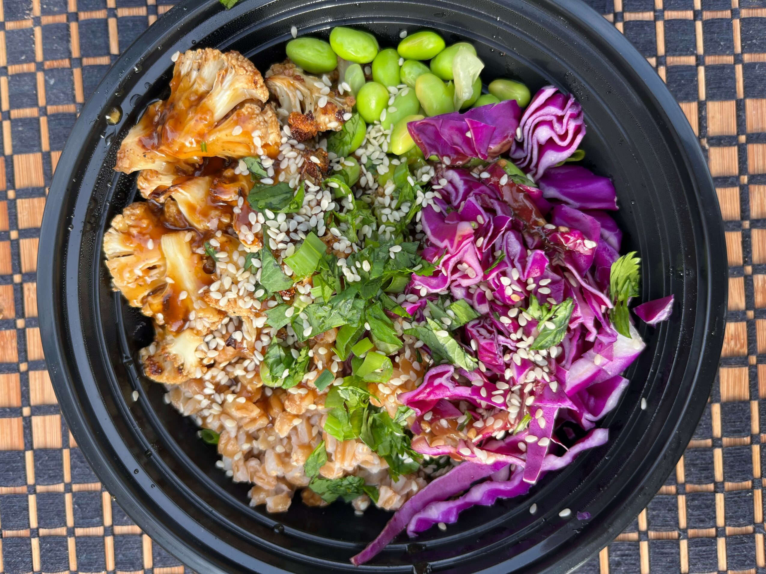 Black bowl with cooked mushrooms, green beans, purple cabbage, and sesame seeds on a woven surface.