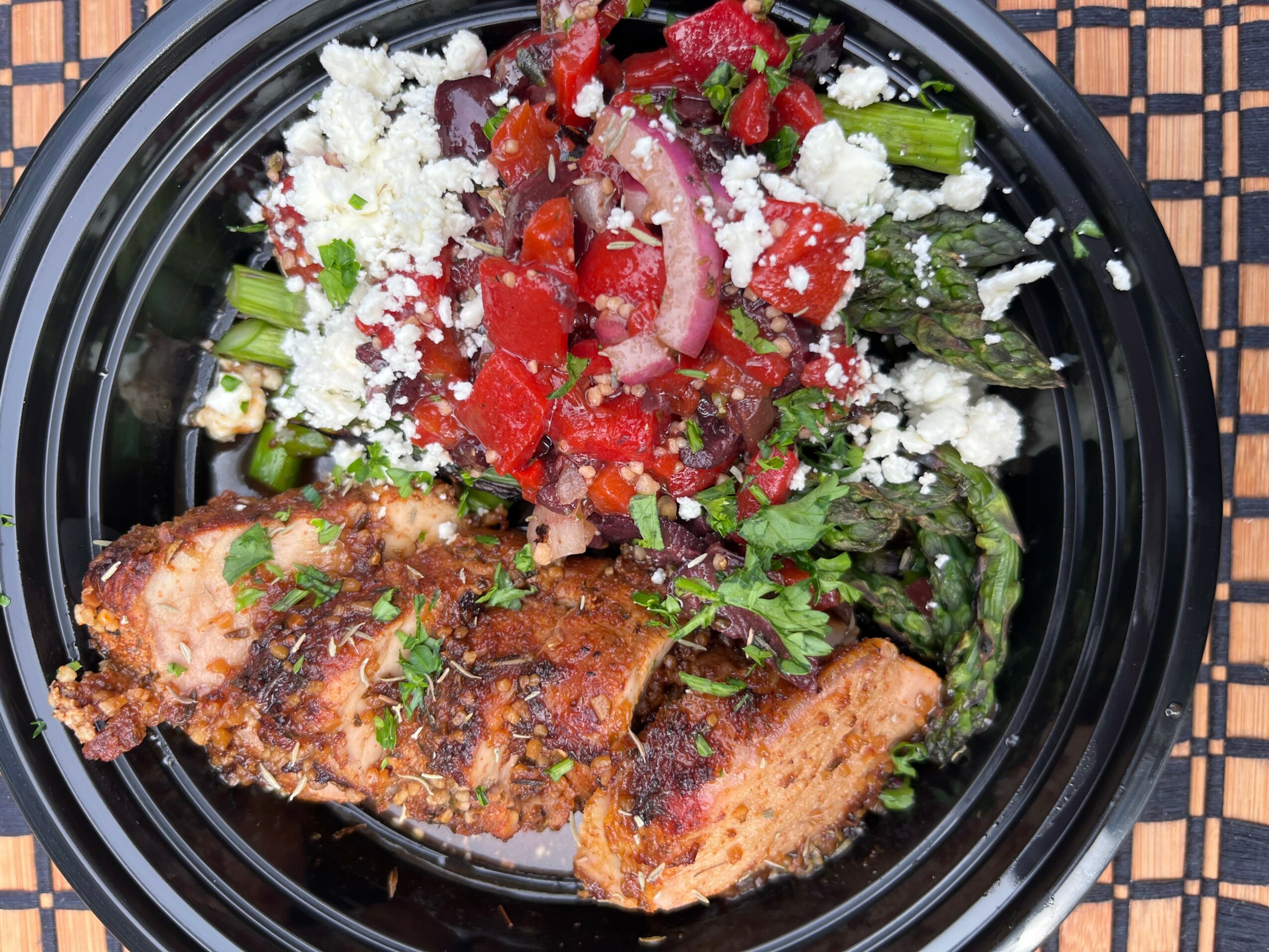 Fried fish fillet with salad including tomatoes, onions, and greens, topped with cheese, on a black plate.