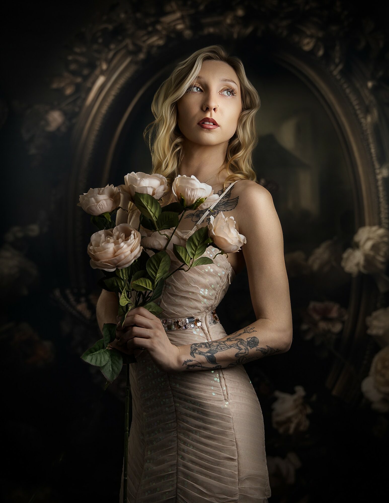 Woman with wavy blonde hair holding a bouquet of pink roses, standing in front of a dark ornate mirror.