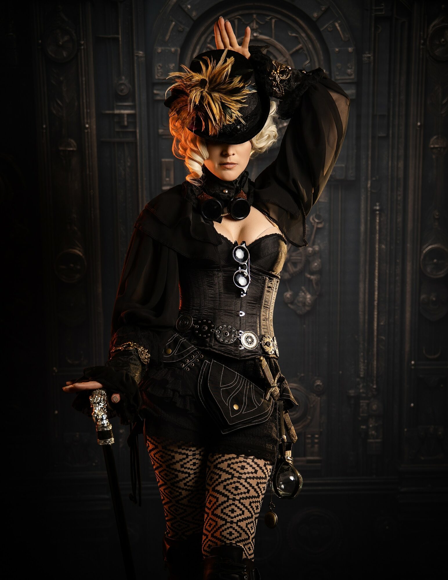 Woman in elaborate costume with feathered hat, mask, and patterned tights, standing in front of dark ornate background.