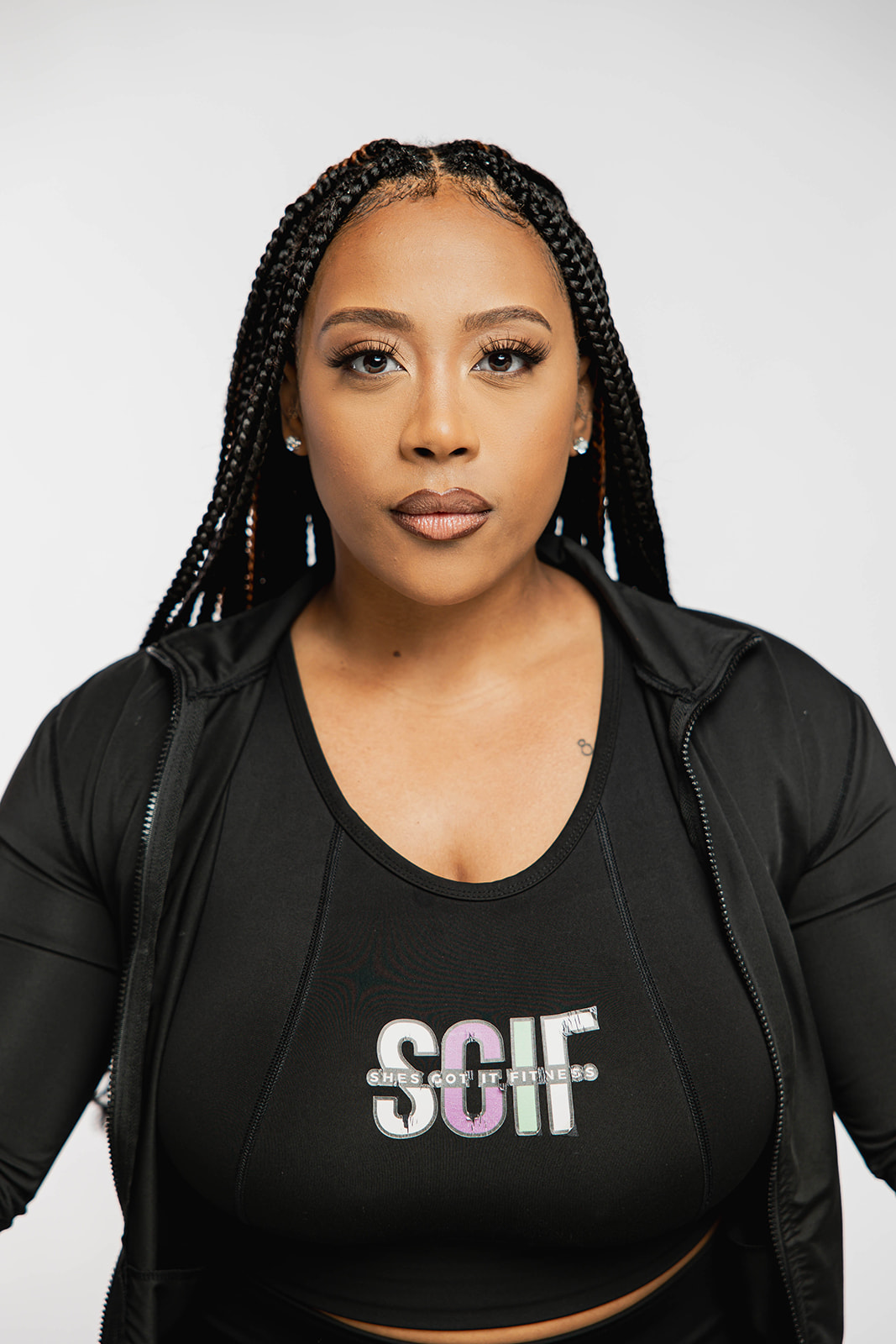 Woman with braided hair wearing a black jacket and shirt with 'SCF' logo, facing forward, neutral expression.