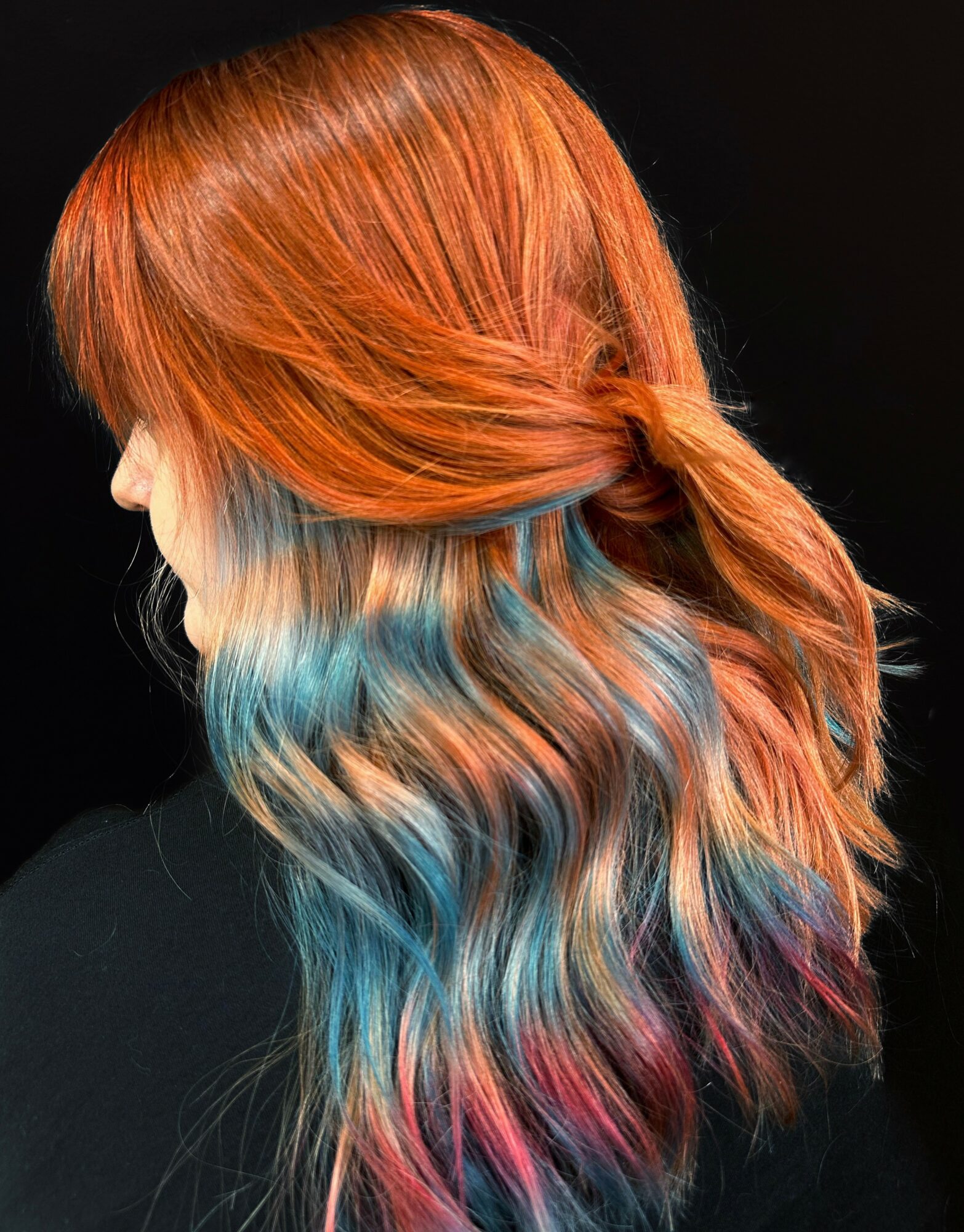 Side view of a person with long, wavy hair dyed in red, blue, and pink colors.