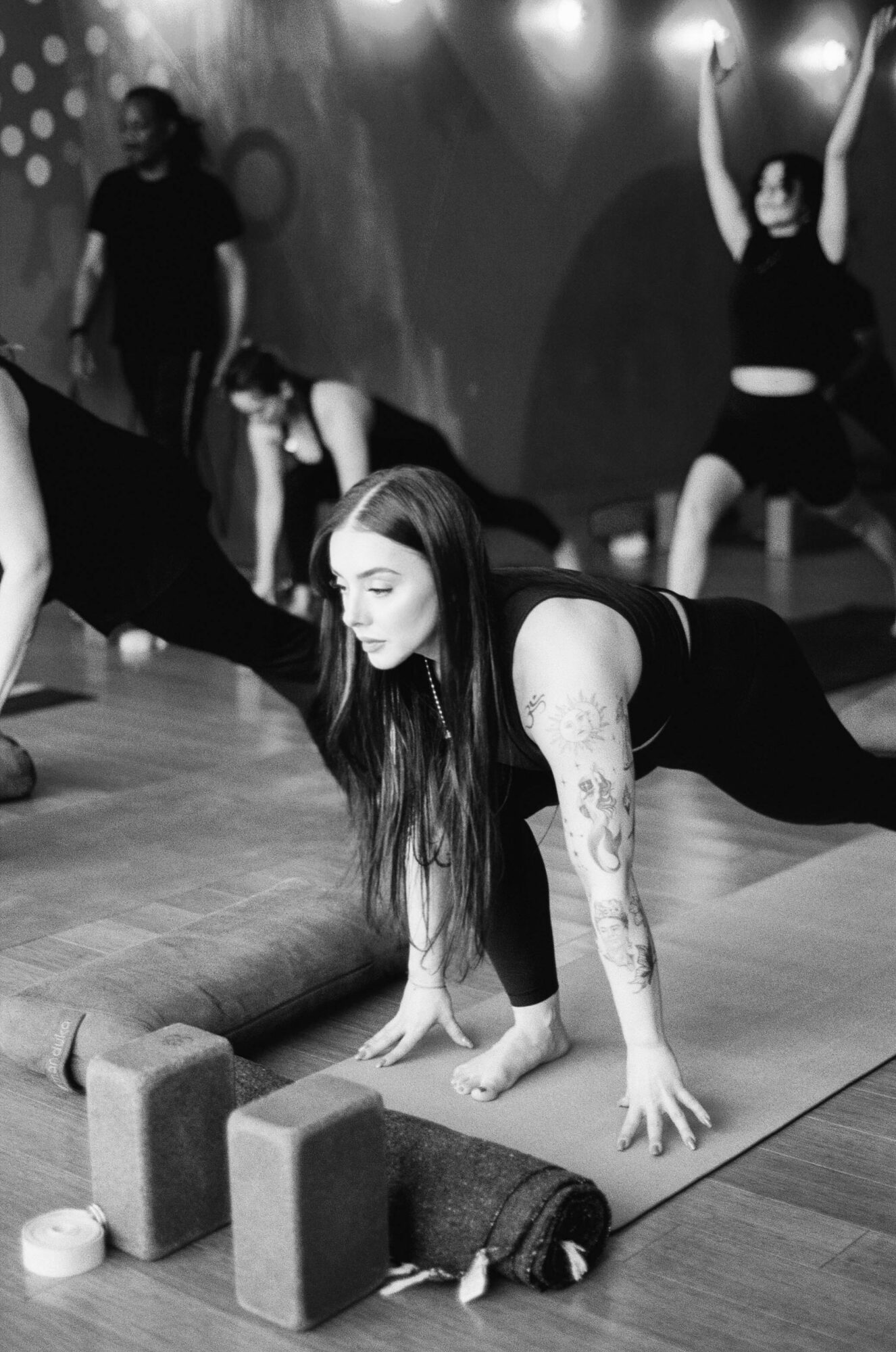Group of people practicing yoga or stretching on mats in a studio, with one woman in foreground doing a side stretch.