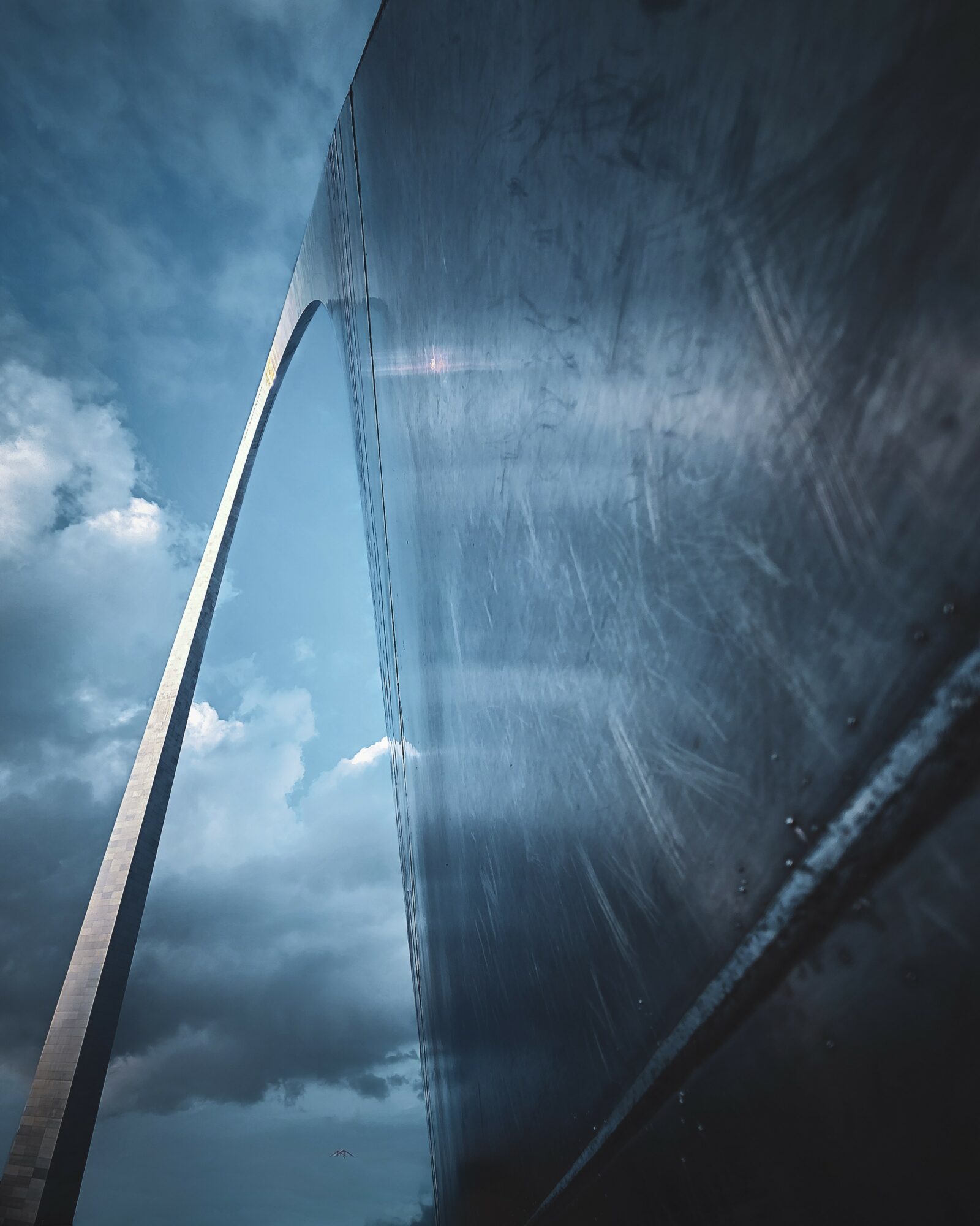A tall, curved structure extends into a cloudy sky, with a reflective surface showing the sky and clouds.