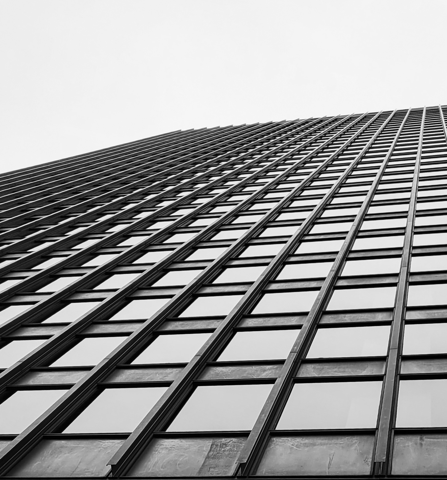 Tall building with glass windows and grid-like structure, viewed from below, reaching into the sky.