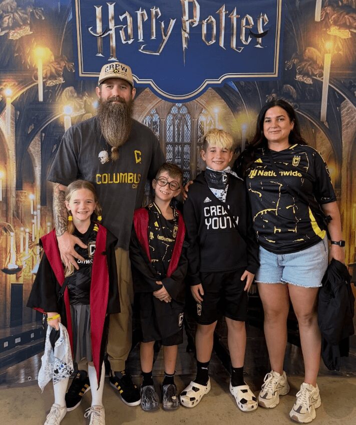 Group of five people, two adults and three children, standing in front of a Harry Potter-themed backdrop, smiling.