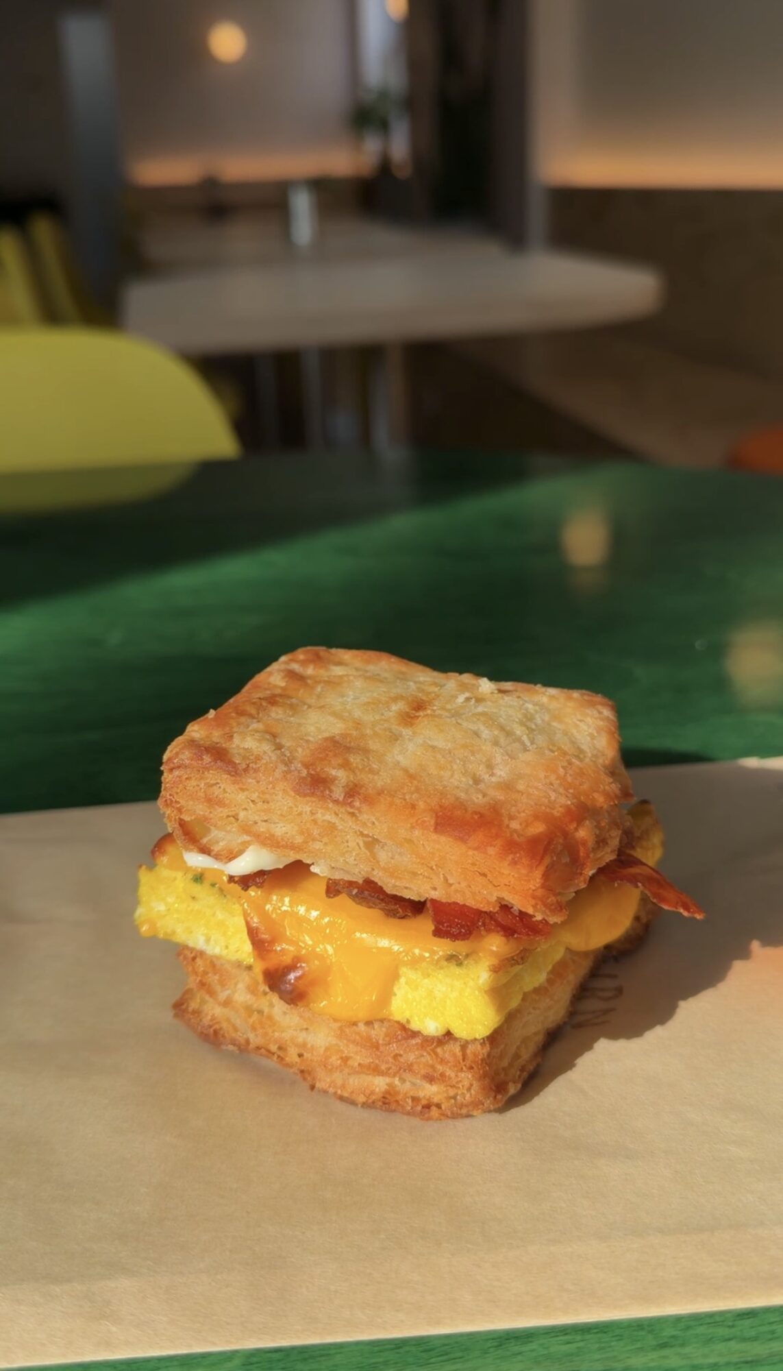Fried chicken sandwich with fried chicken, yellow cheese, and breaded bun on parchment paper, in a restaurant setting.