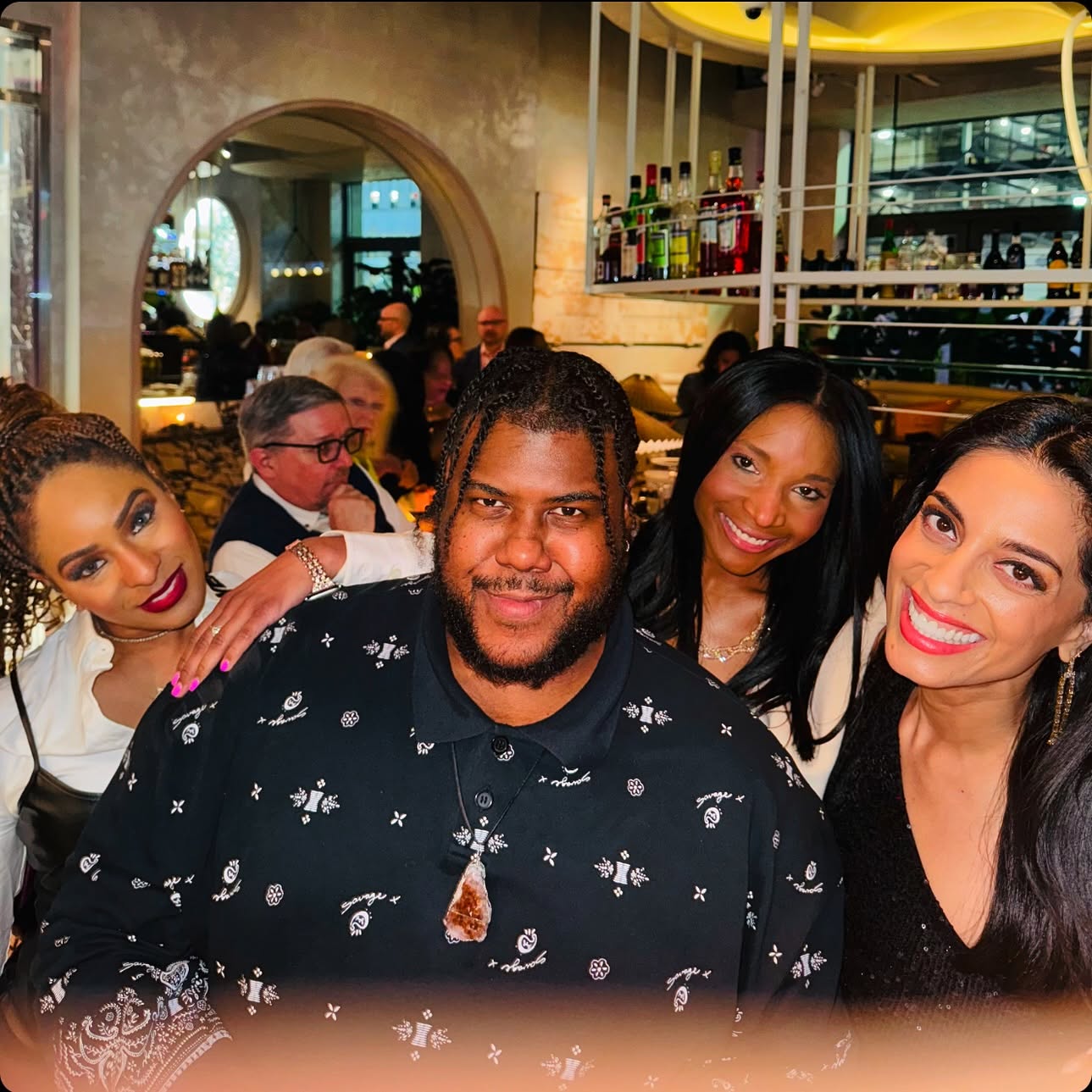 Four people smiling together in a restaurant, with a bar and mirror in the background.