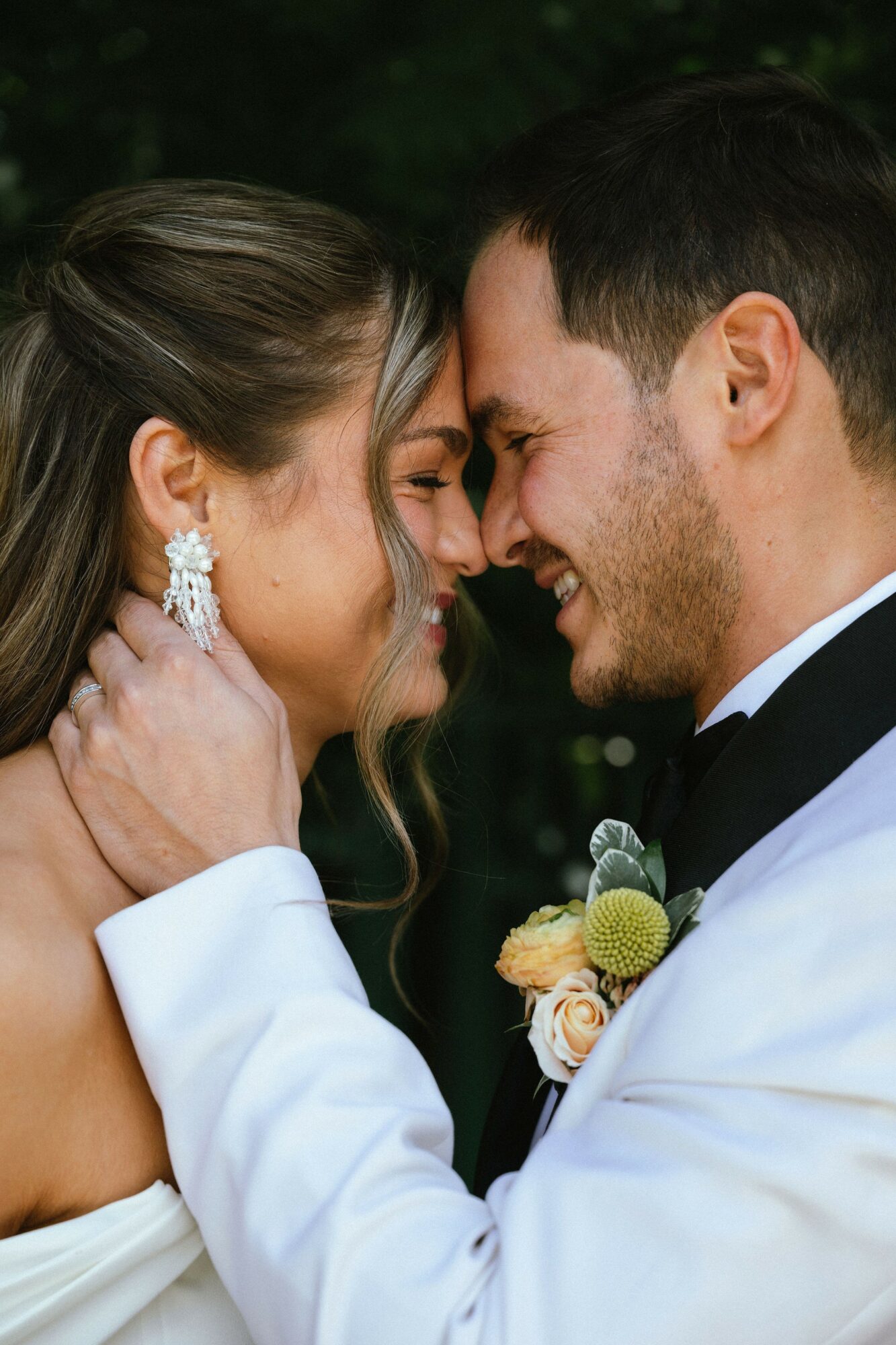 Close-up of a couple smiling with foreheads touching, outdoors, wedding attire, joyful expression.