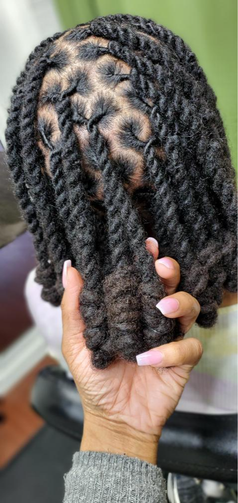 Hand holding a person's braided hairstyle with thick, textured twists, against a blurred background.