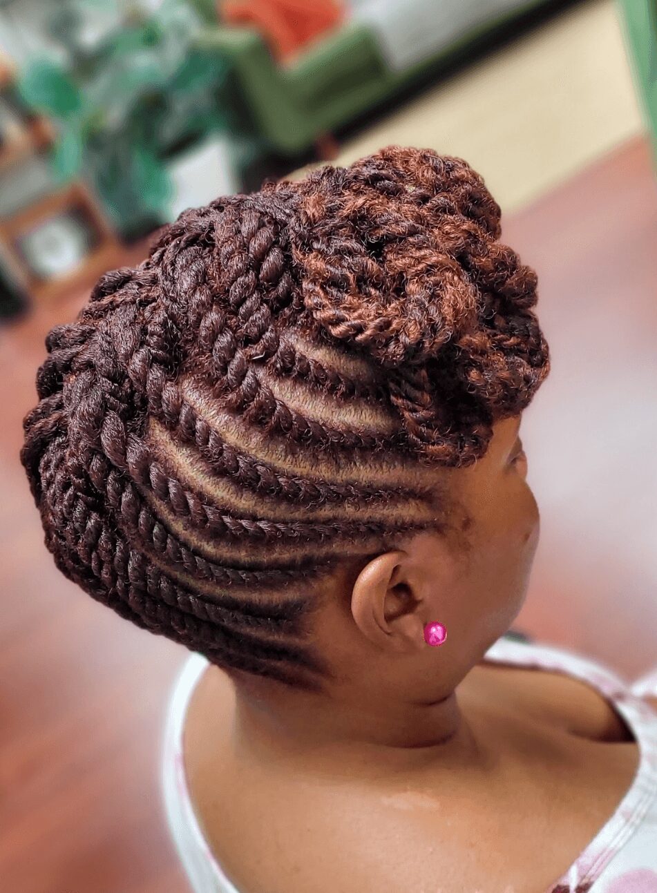 Side view of a woman with intricately styled braided hair in a bun, wearing pink earrings, indoors.