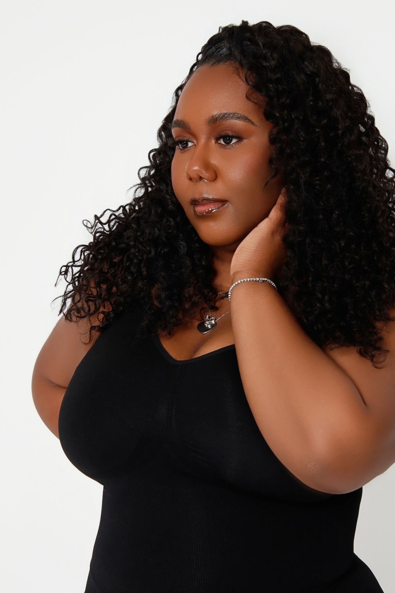 Woman with curly hair wearing a black top, touching her face, against a white background.