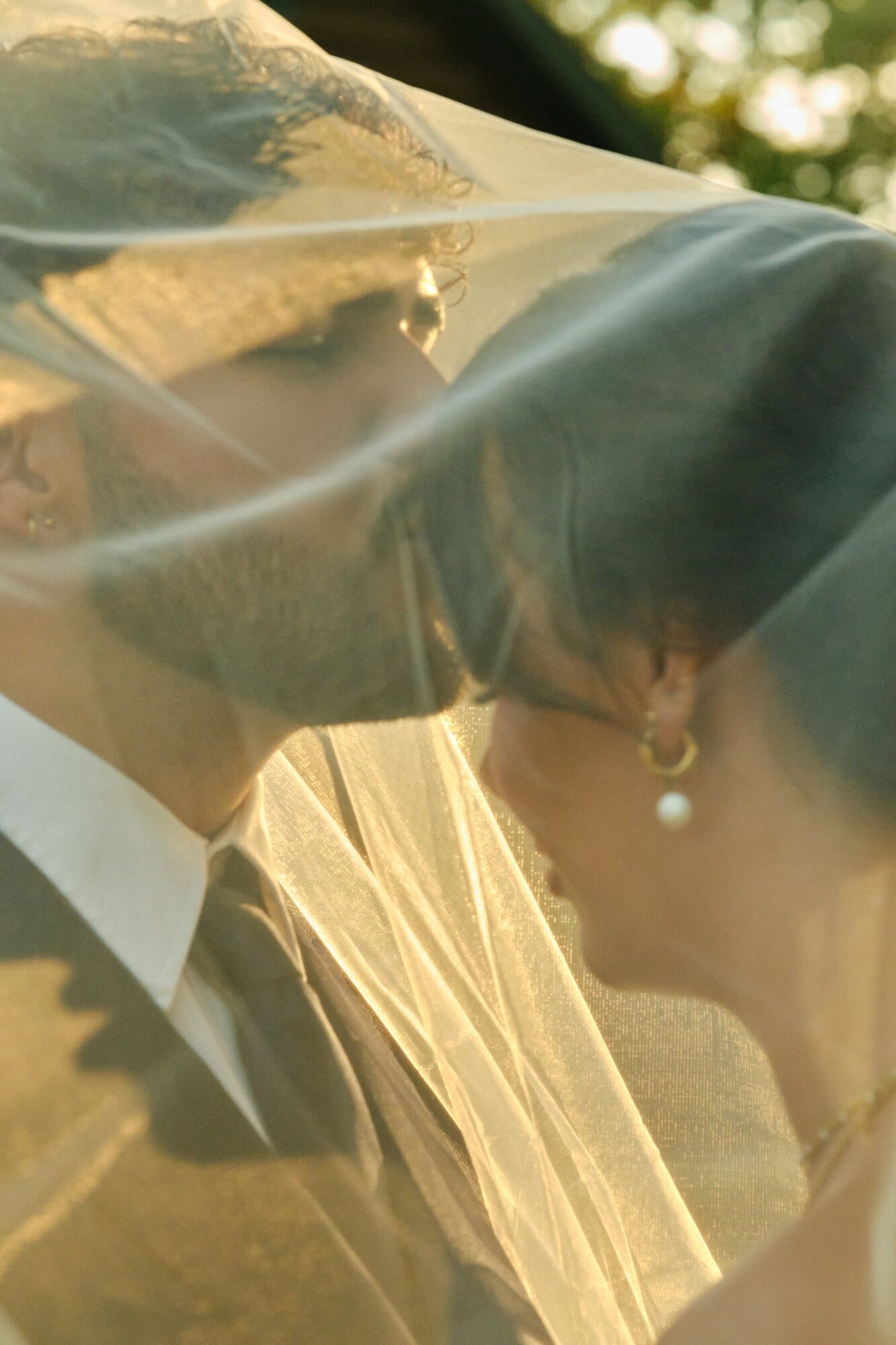 A couple with a veil between them, outdoors during sunset, close-up of faces and veil, romantic scene.