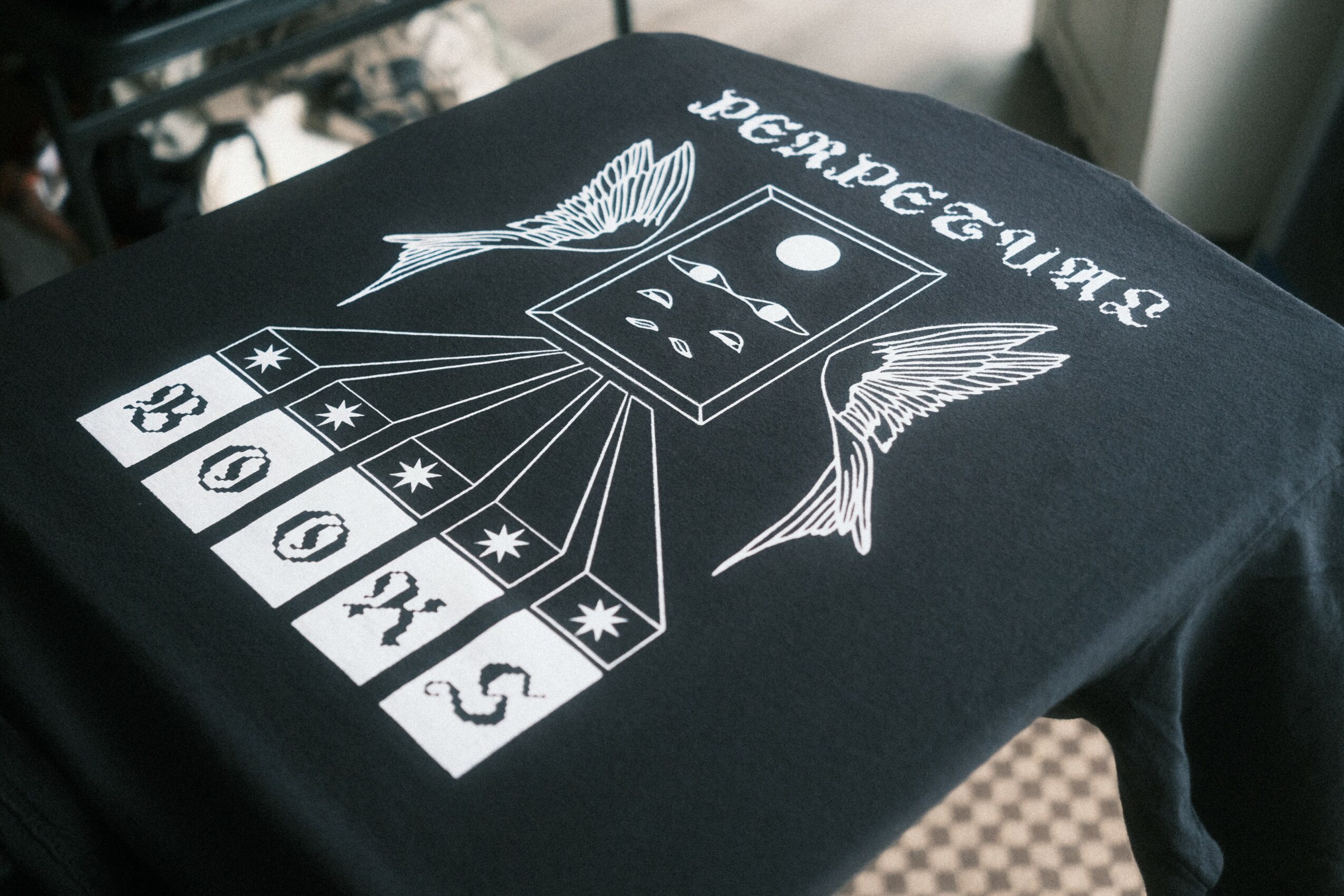 Black T-shirt with white graphic of a fish, a moon, and a grid of numbers and symbols, with text upside down.