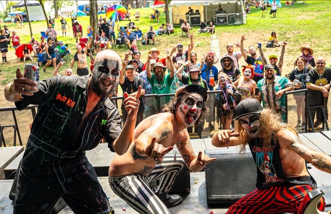 Clowns and performers in costumes pose in front of a crowd at an outdoor event, with people watching in the background.