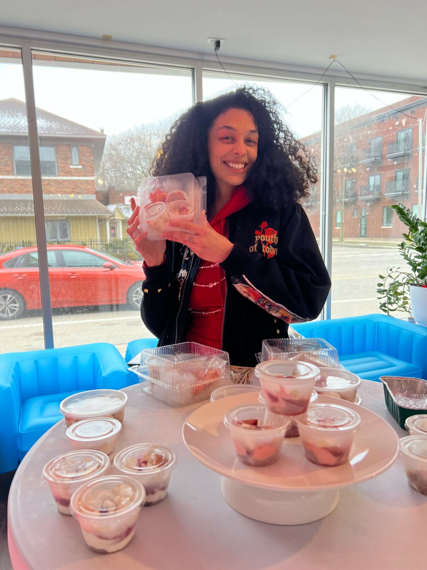 Woman with curly hair pouring a drink at a table with cups and a blue inflatable pool in the background.