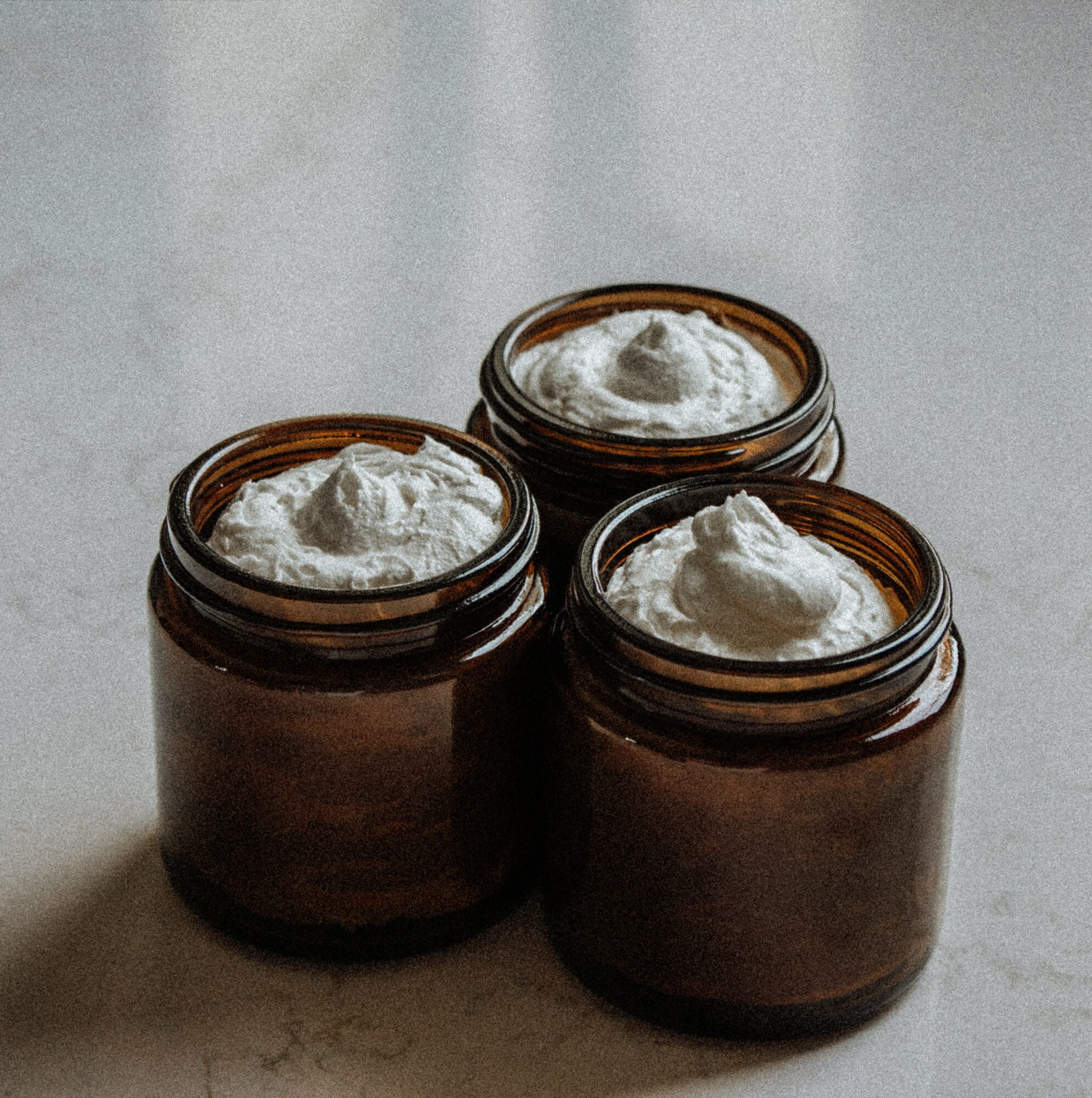 Three brown jars filled with white cream or substance, placed on a light-colored surface.
