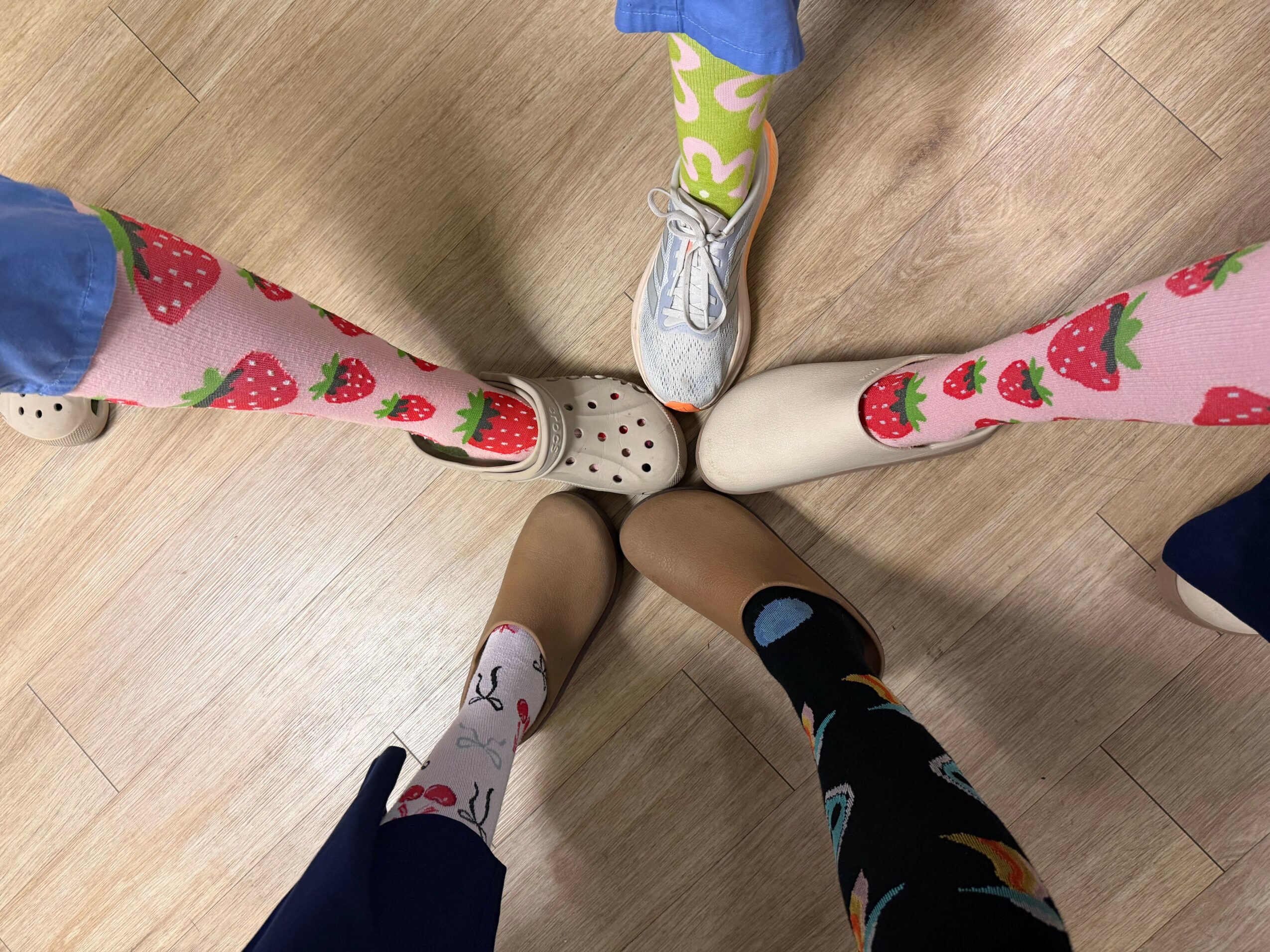 Five people stand in a circle, each wearing colorful socks with different patterns, on a wooden floor.