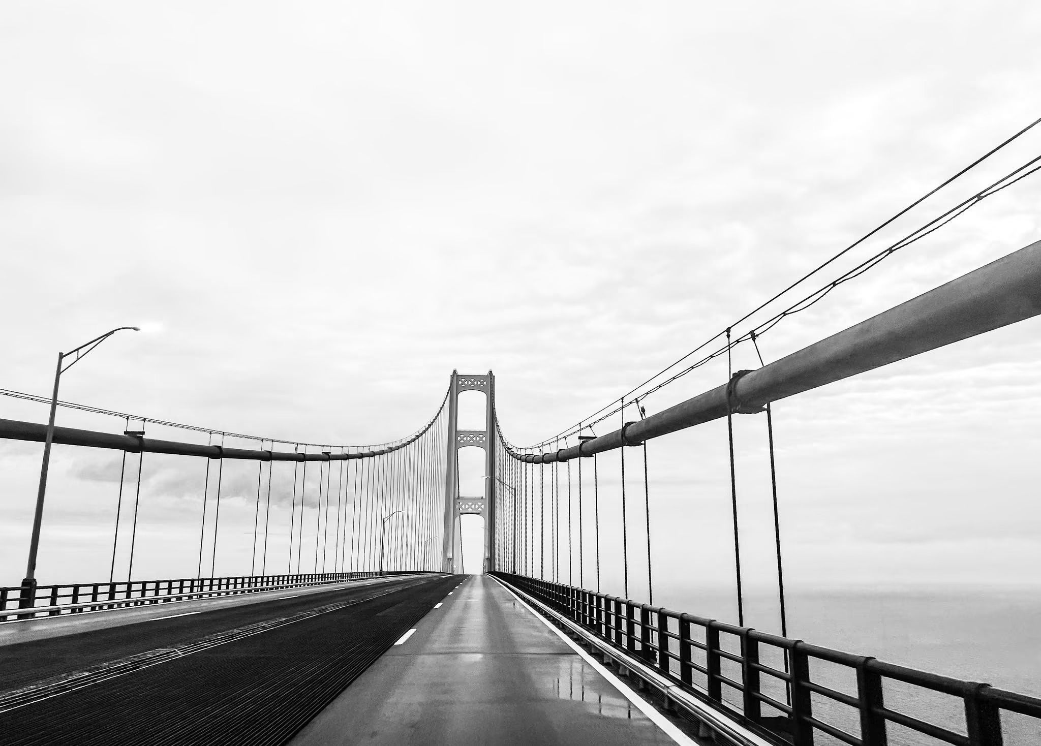 View of a suspension bridge with towers and cables, extending into the distance under a cloudy sky.